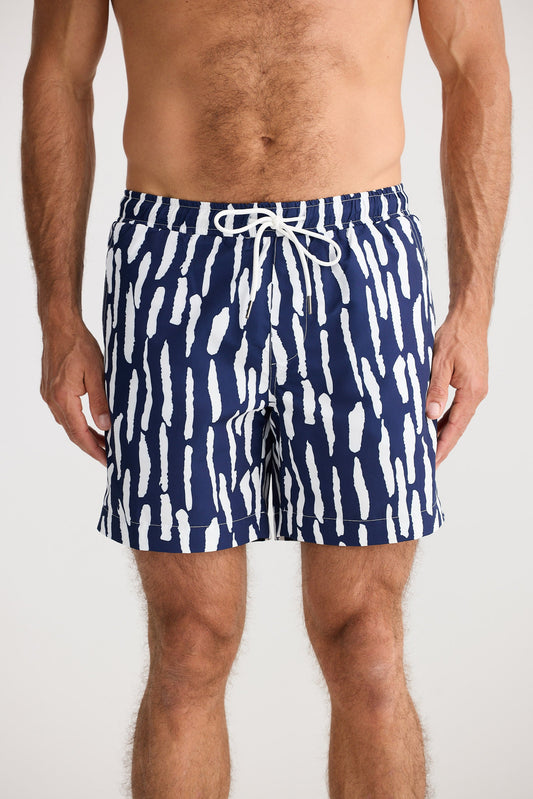 Person wearing navy swim shorts with white abstract pattern on a plain background