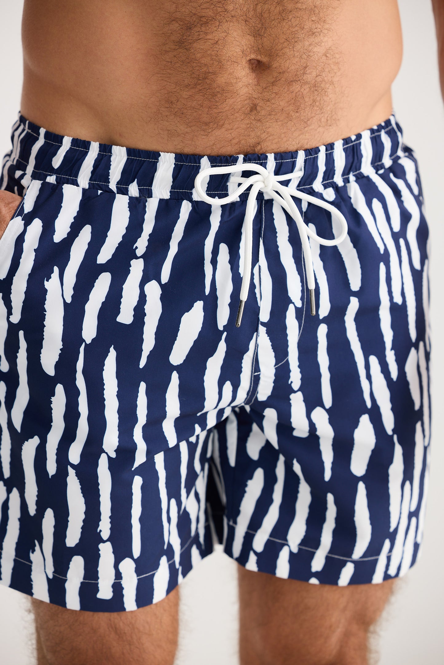 Navy blue swim shorts with white abstract pattern worn by a person on a white background