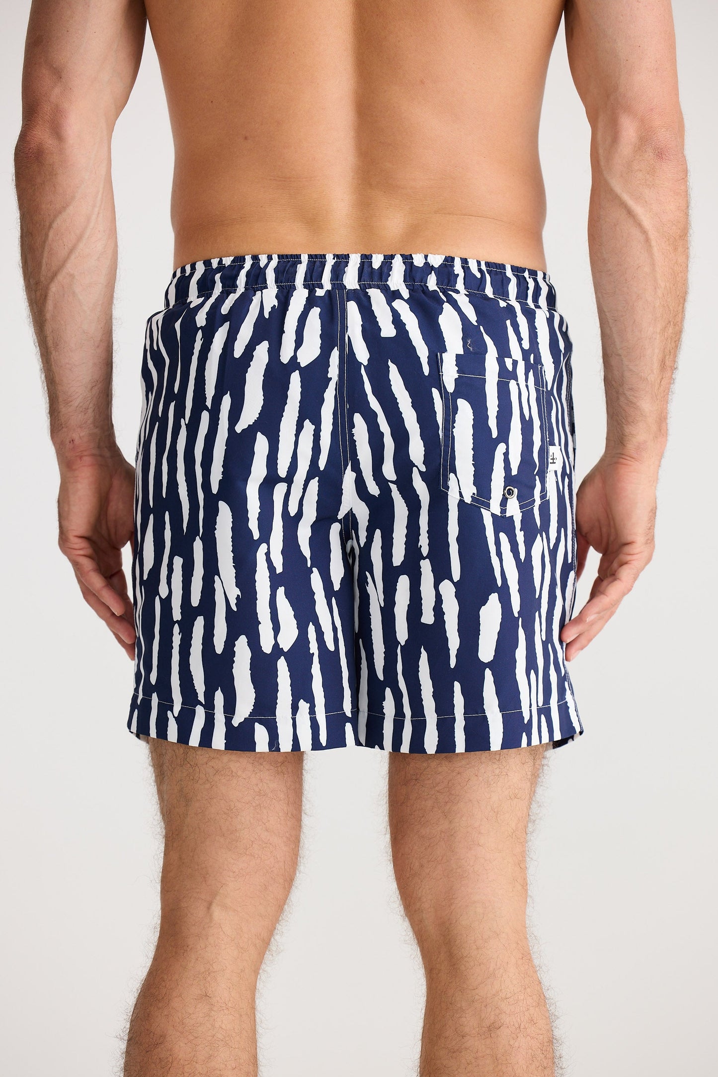 Person wearing navy swim shorts with white abstract pattern on a plain background