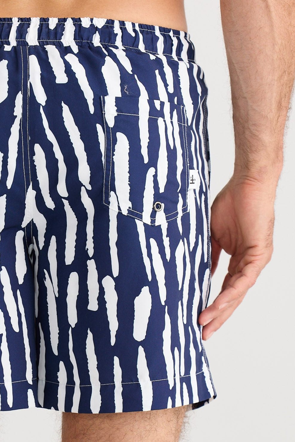 Person wearing navy swim shorts with white abstract pattern on a plain background