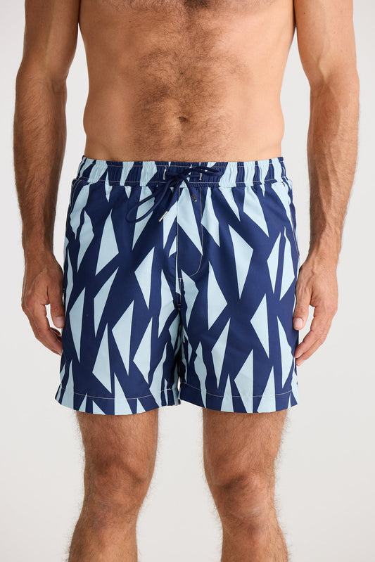 Man wearing blue and white patterned swim shorts on a plain background