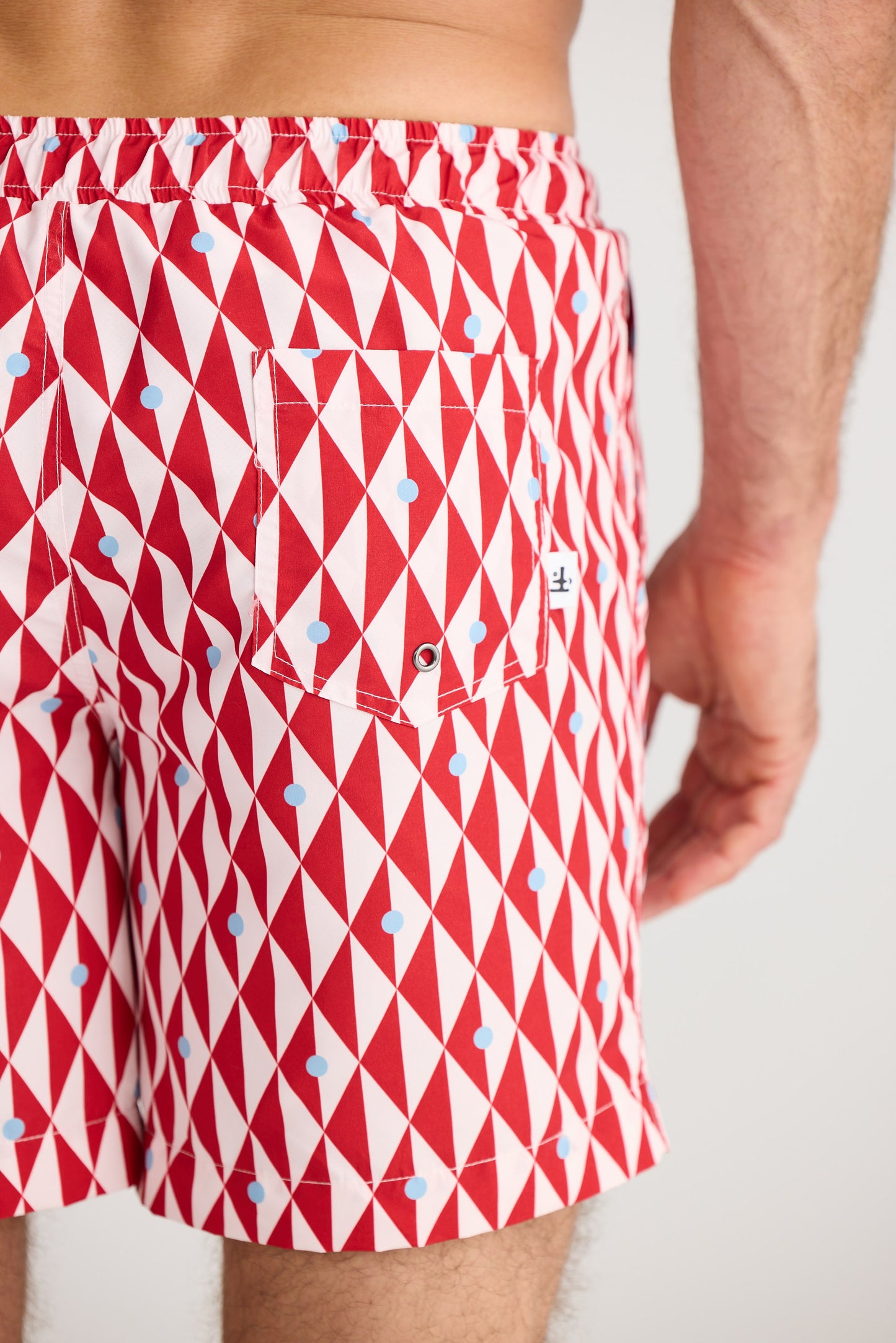 Red and white geometric patterned swim shorts on a plain background