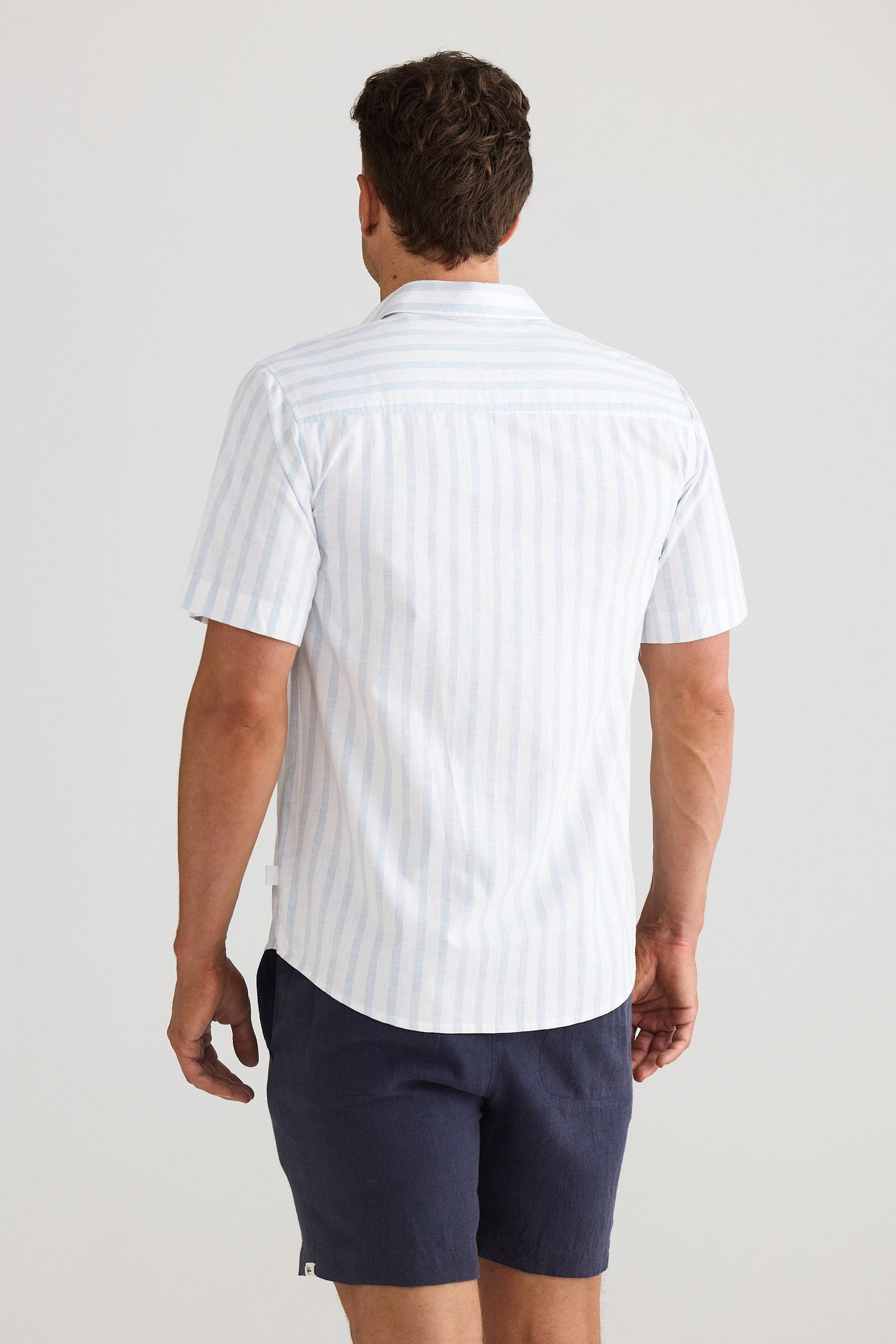 Man wearing a white striped shirt and navy shorts on a plain background