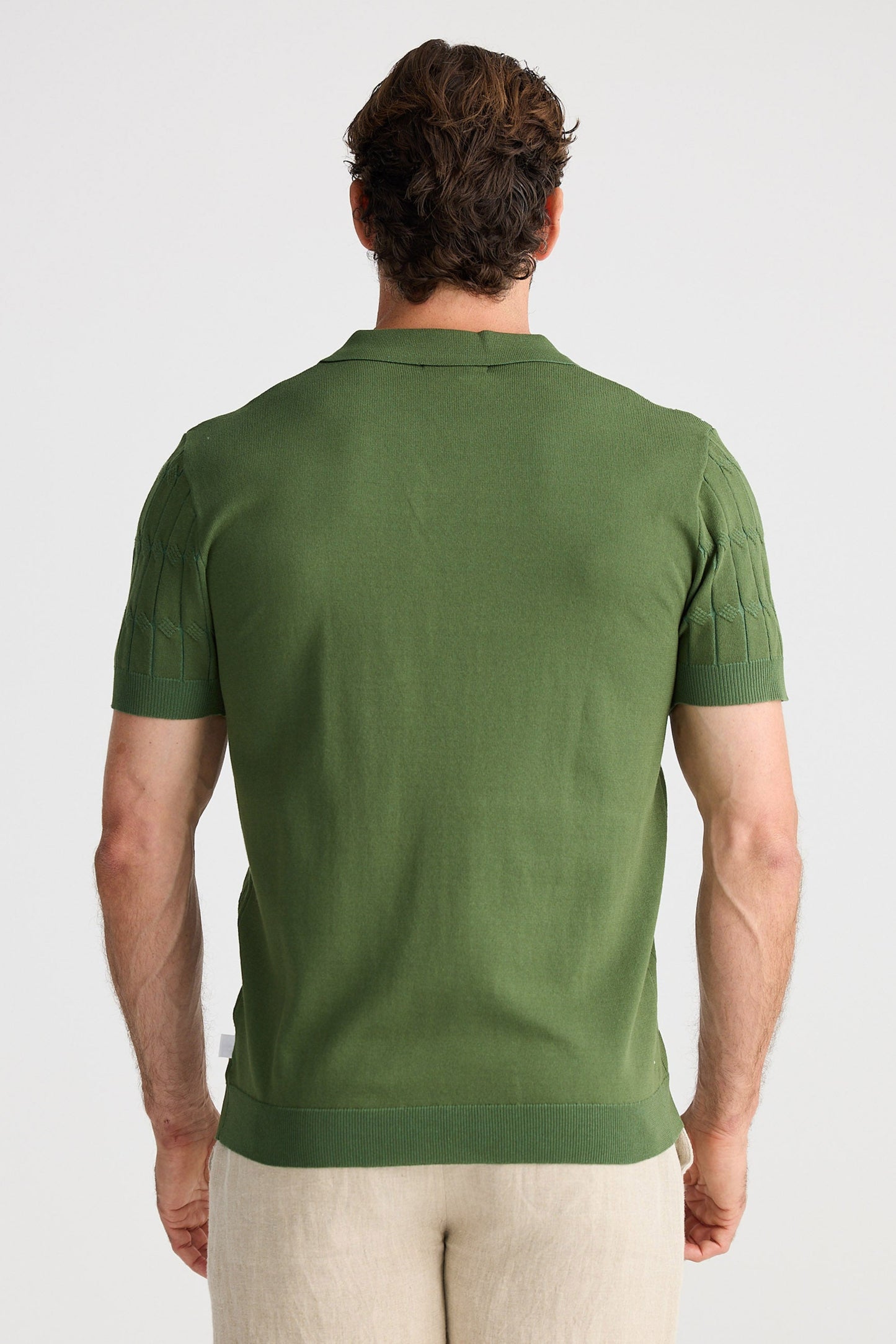Man wearing a green polo shirt and beige shorts on a white background