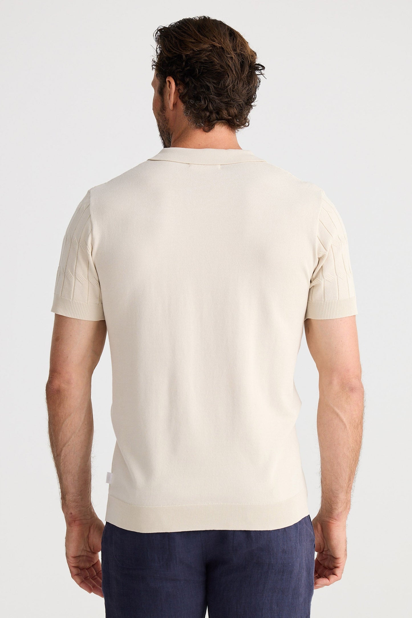Man wearing a beige polo shirt and navy shorts on a white background