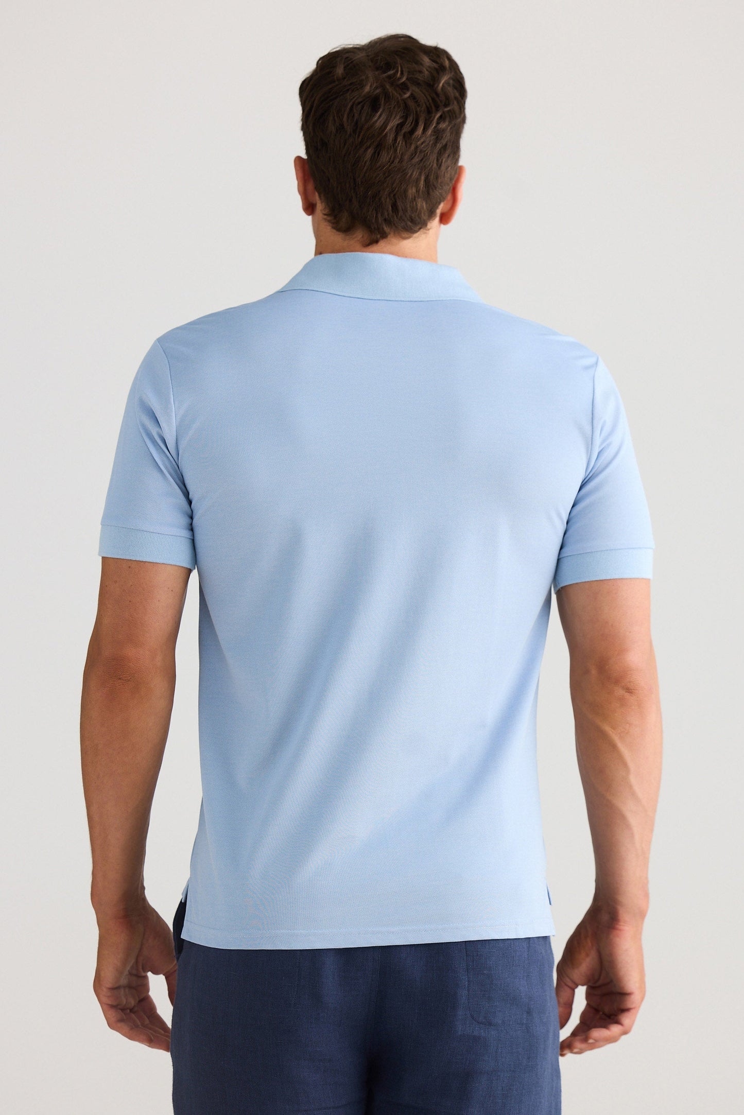 Man wearing a light blue polo shirt and dark blue shorts on a plain background