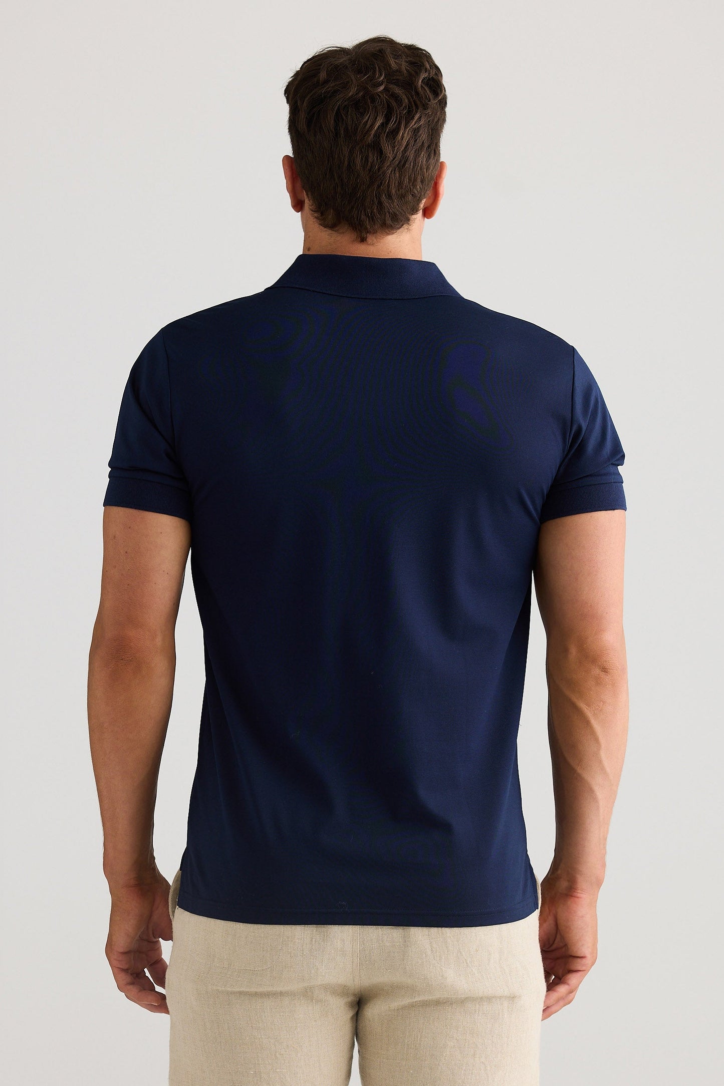 Man wearing a navy blue polo shirt and beige pants on a light gray background