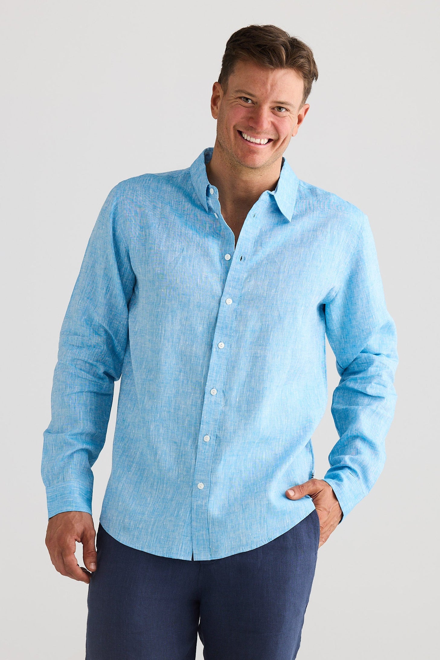 Man wearing a light blue button-up shirt and navy shorts on a white background