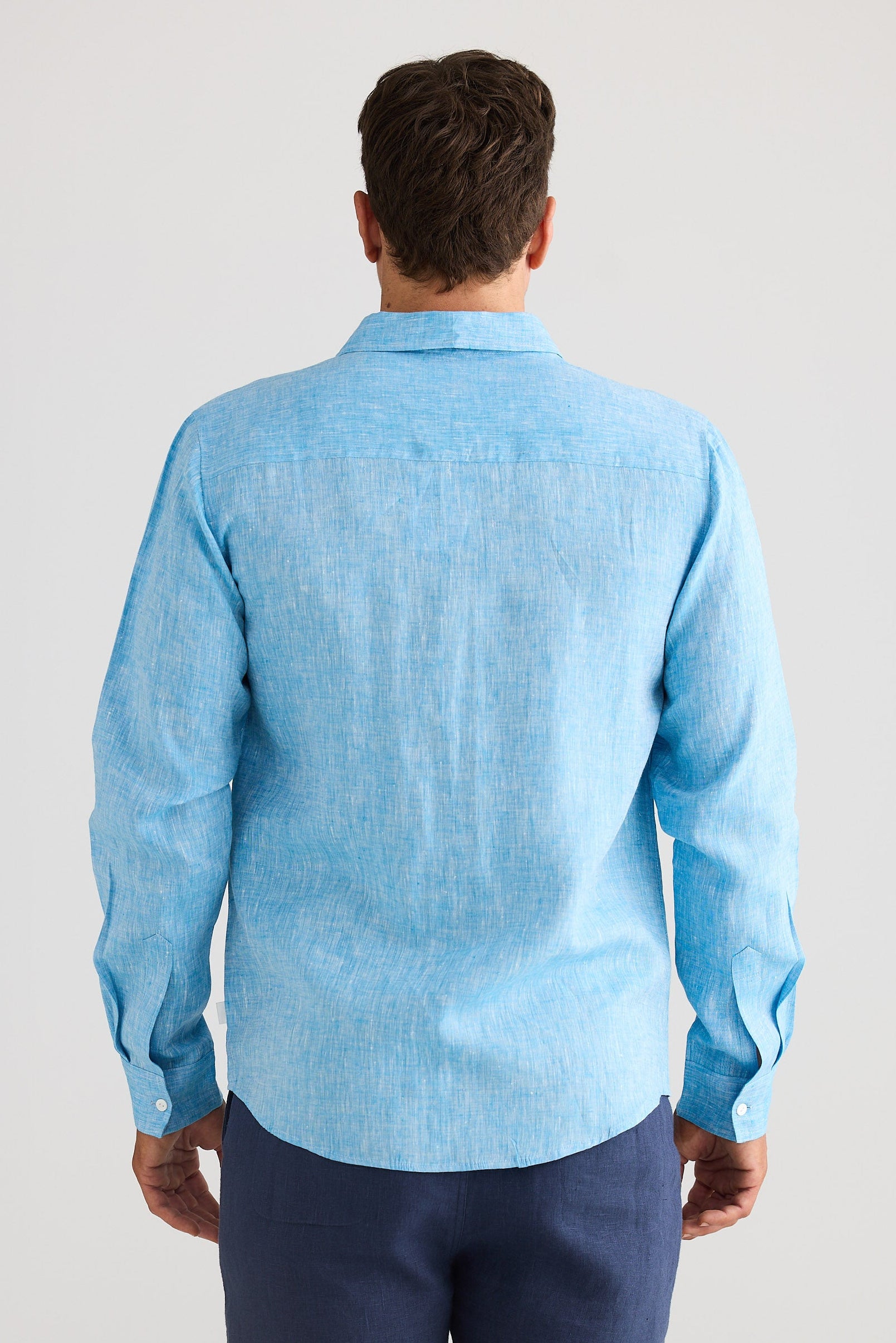 Man wearing a light blue shirt and navy shorts on a plain background