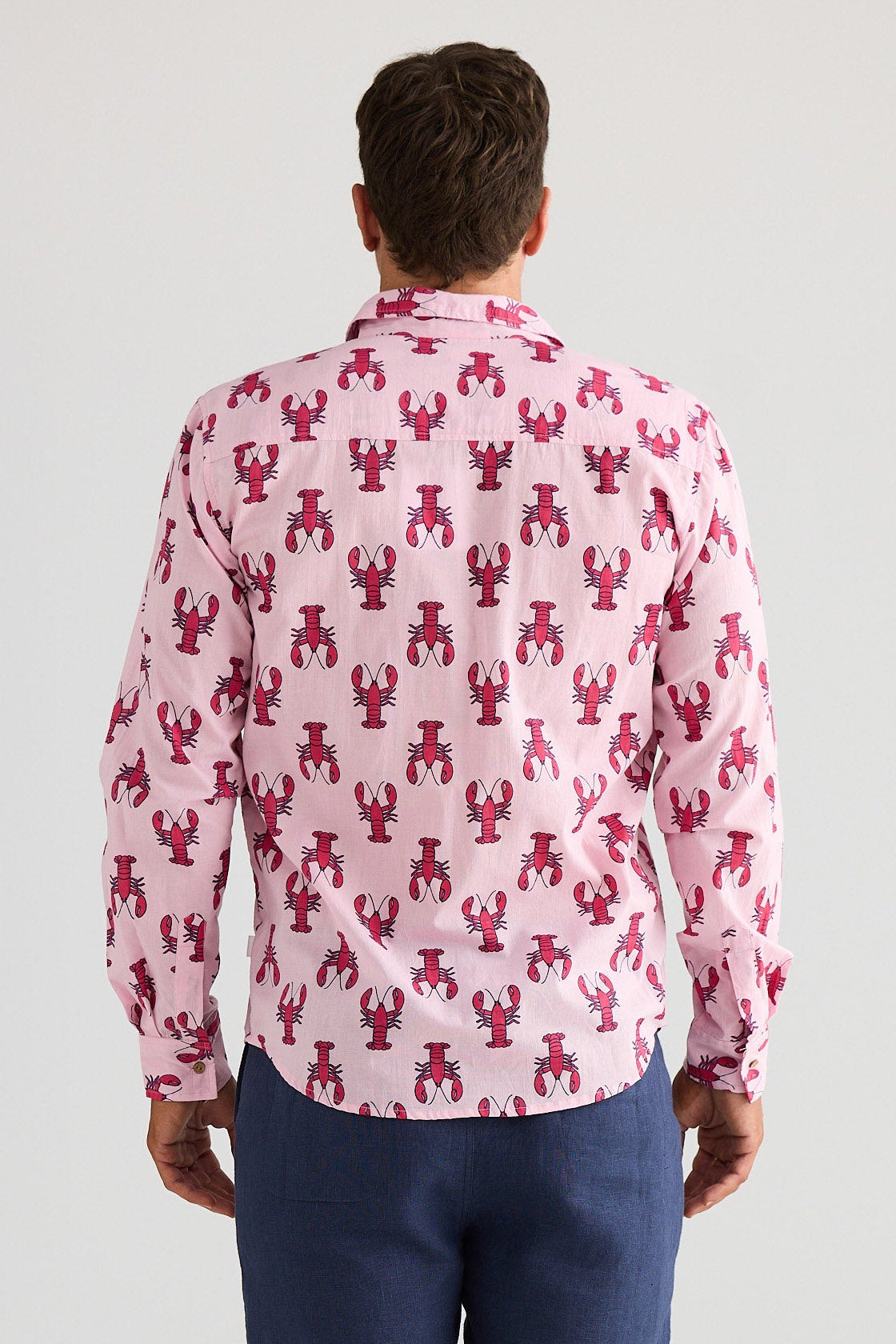 Man wearing a pink shirt with red lobster pattern and blue shorts on a white background