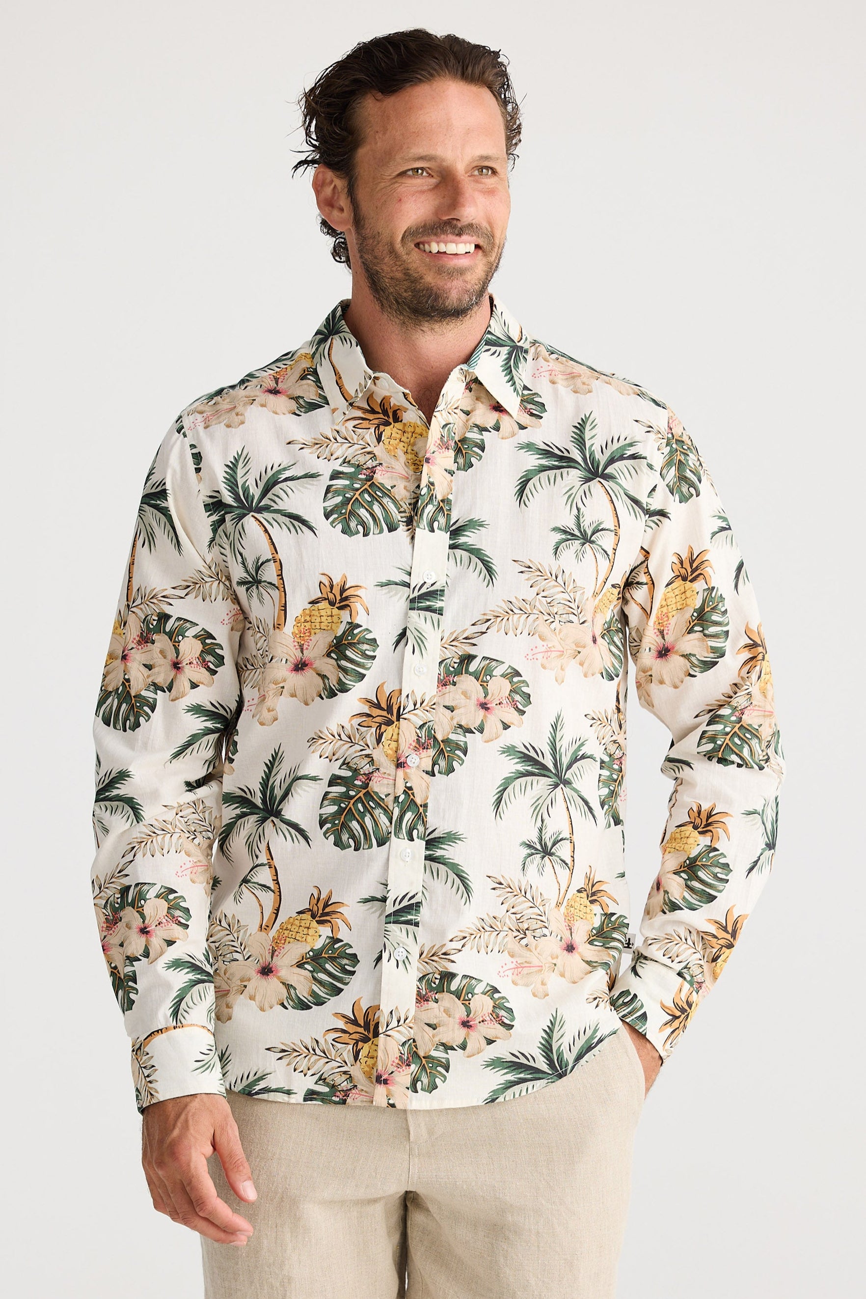 Man wearing a tropical patterned shirt and beige shorts on a white background
