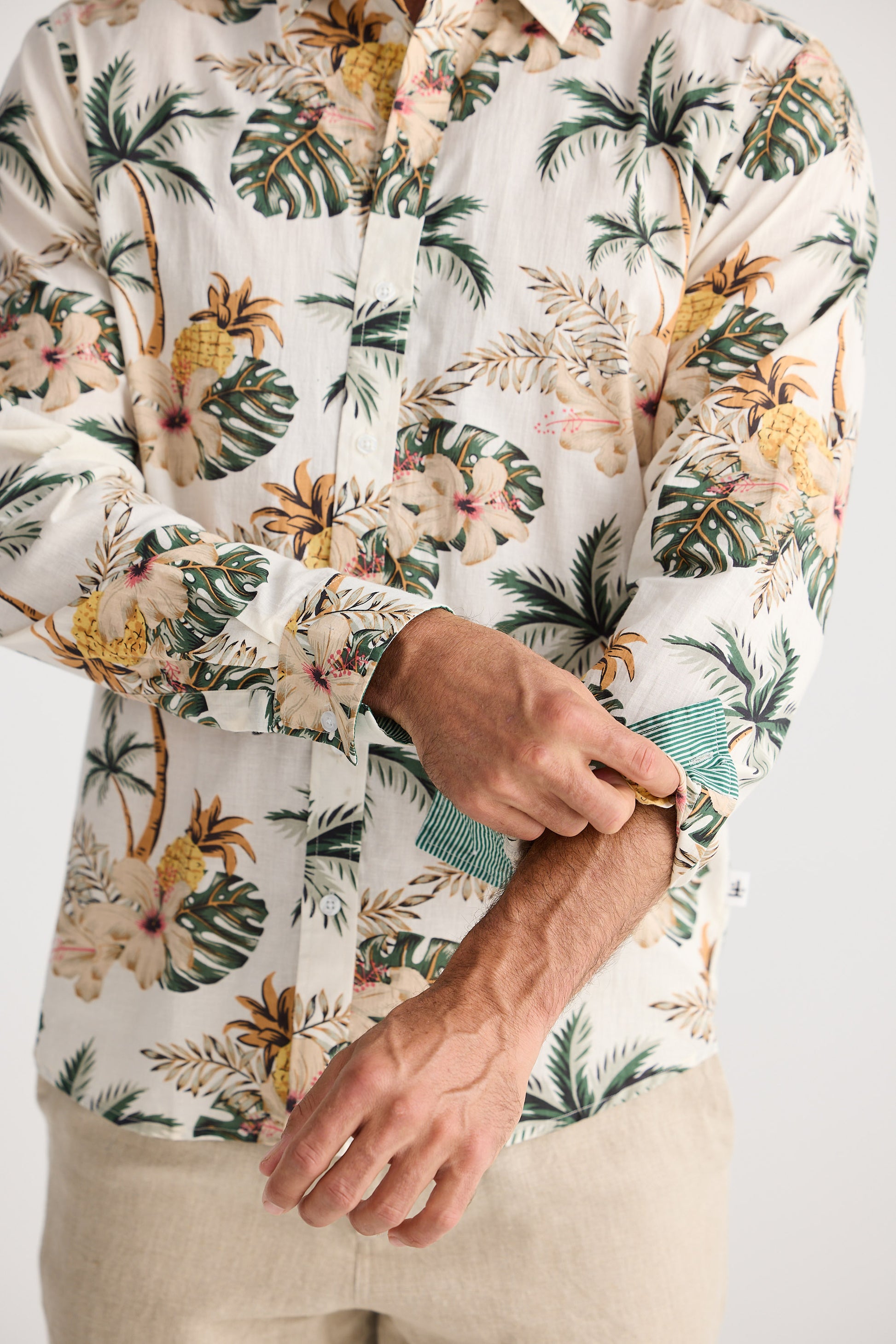 Person wearing a tropical floral shirt with beige pants on a plain background