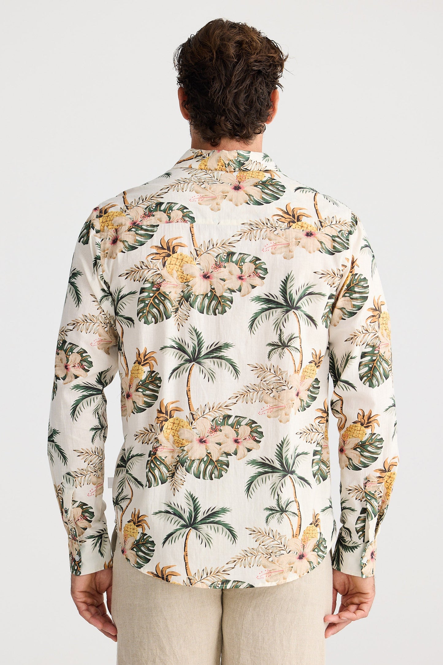 Man wearing a tropical floral shirt with palm trees and flowers on a plain background