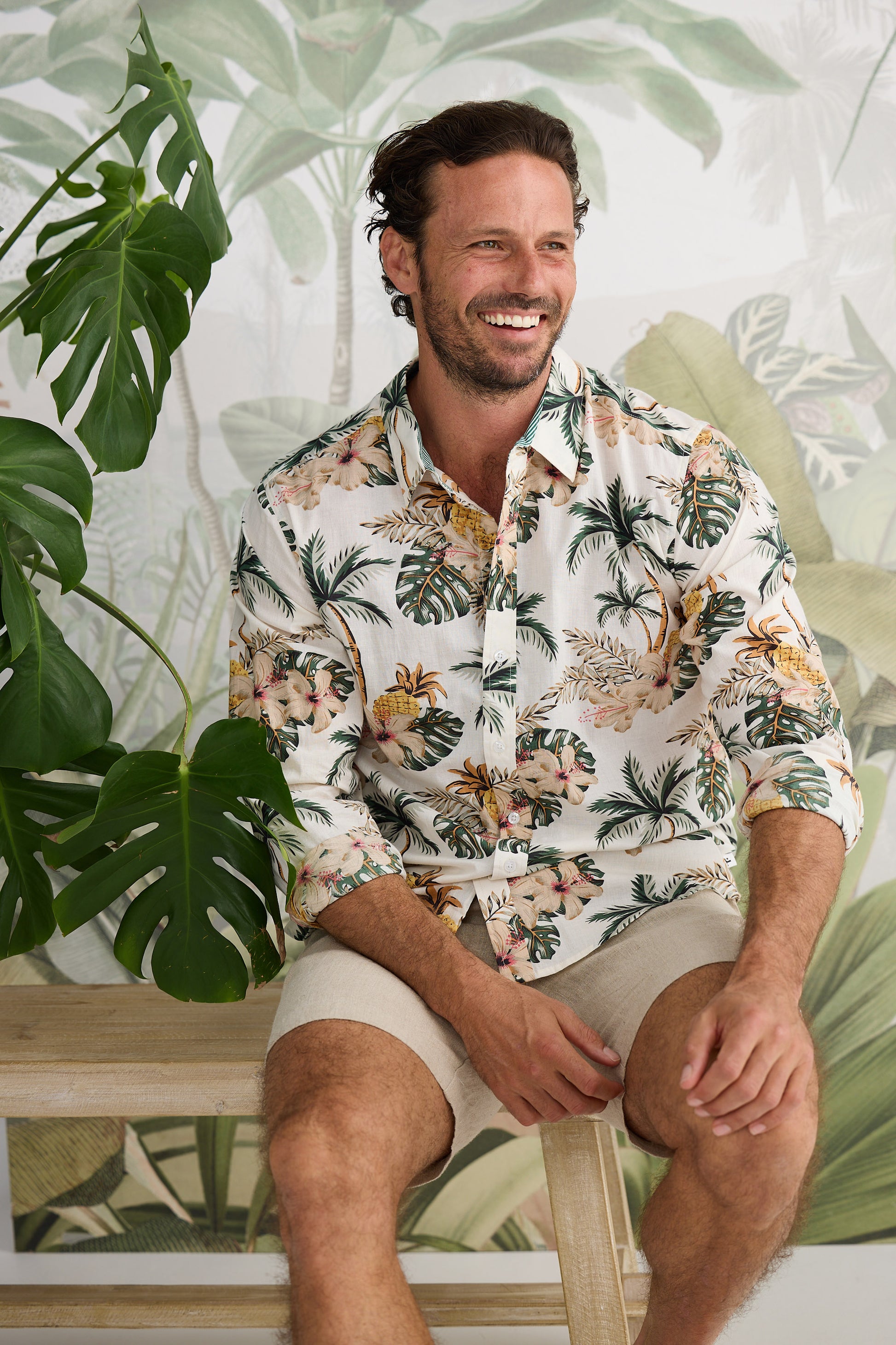 Man wearing a tropical patterned shirt sitting in a room with plants