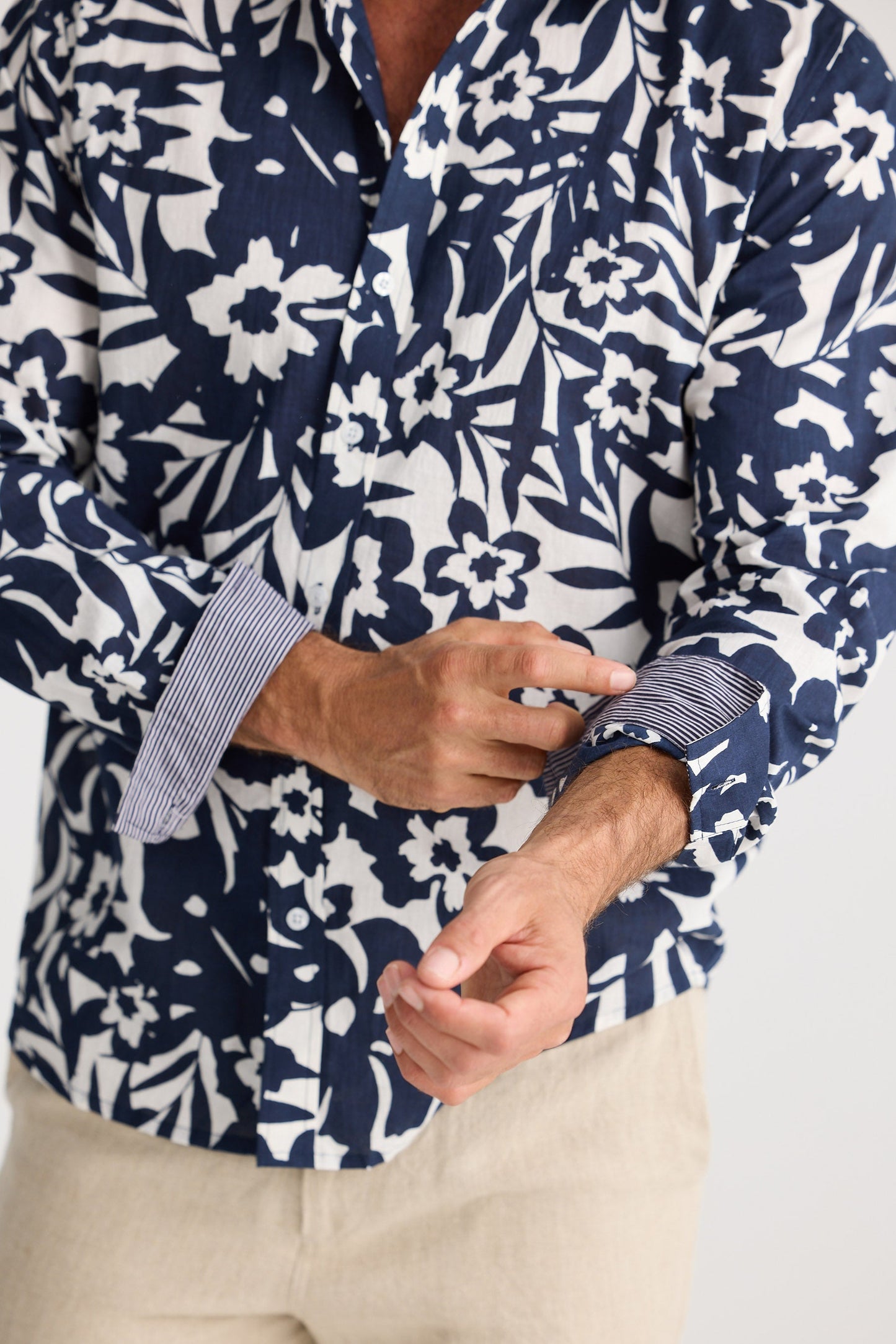 Person wearing a navy and white floral patterned shirt with beige pants on a white background
