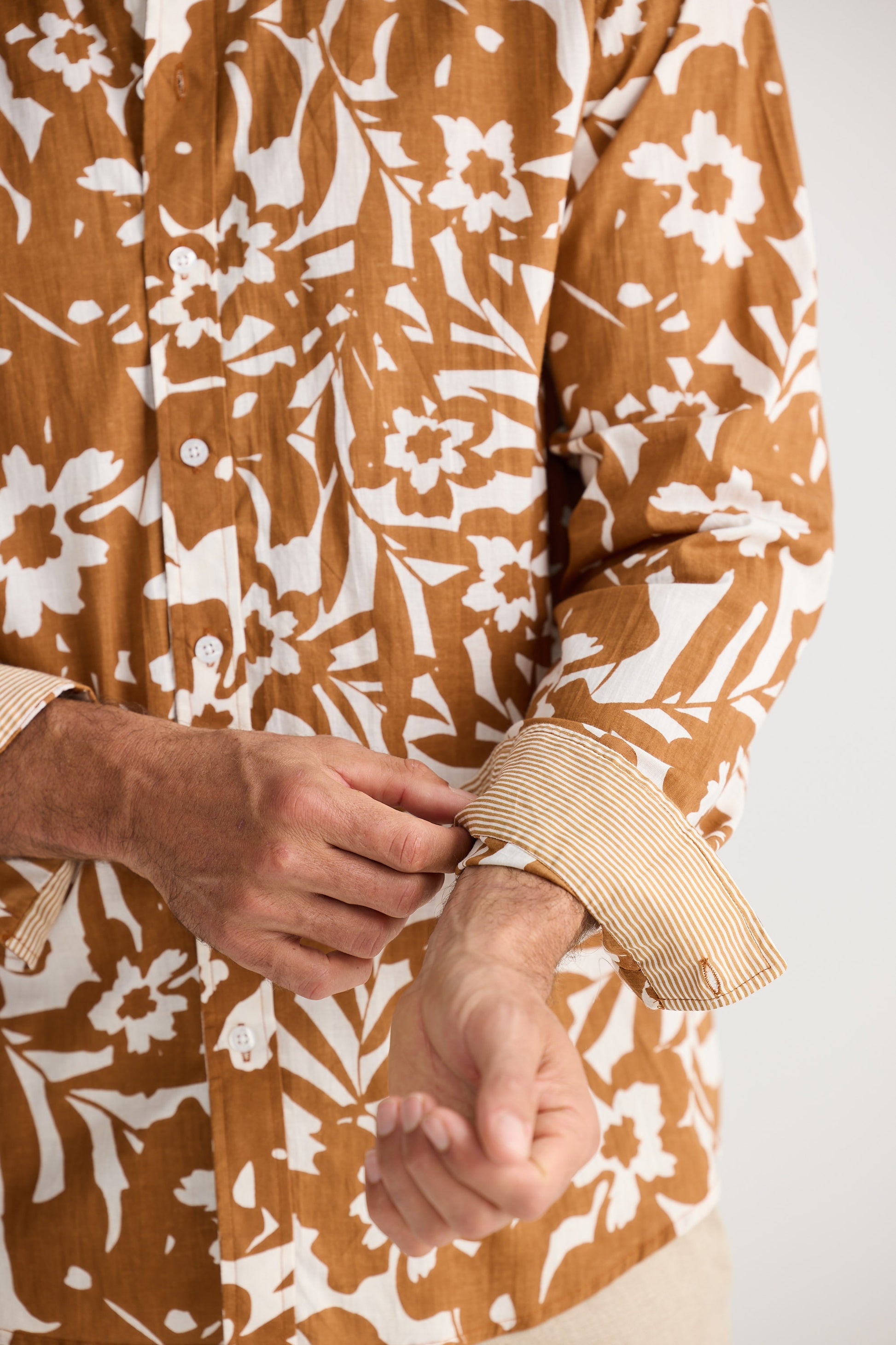 Close-up of a person wearing a brown floral patterned shirt with rolled-up sleeves.