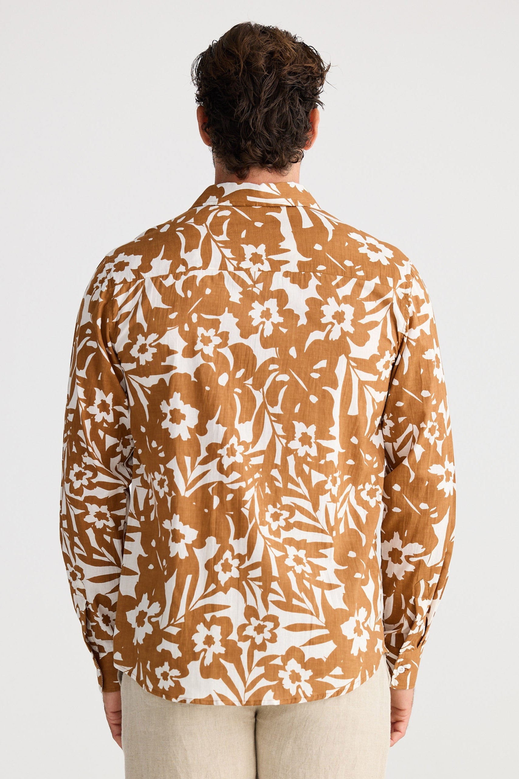 Person wearing a patterned shirt and beige shorts on a white background