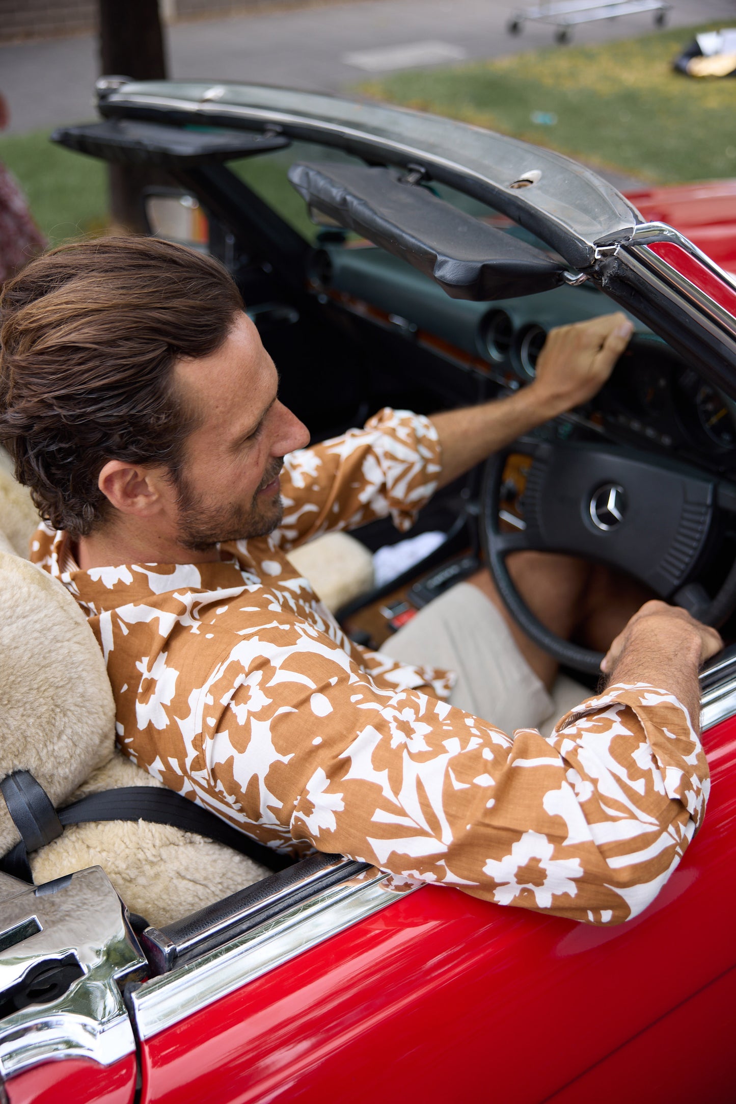 Man sitting in a red convertible car with a teddy bear.
