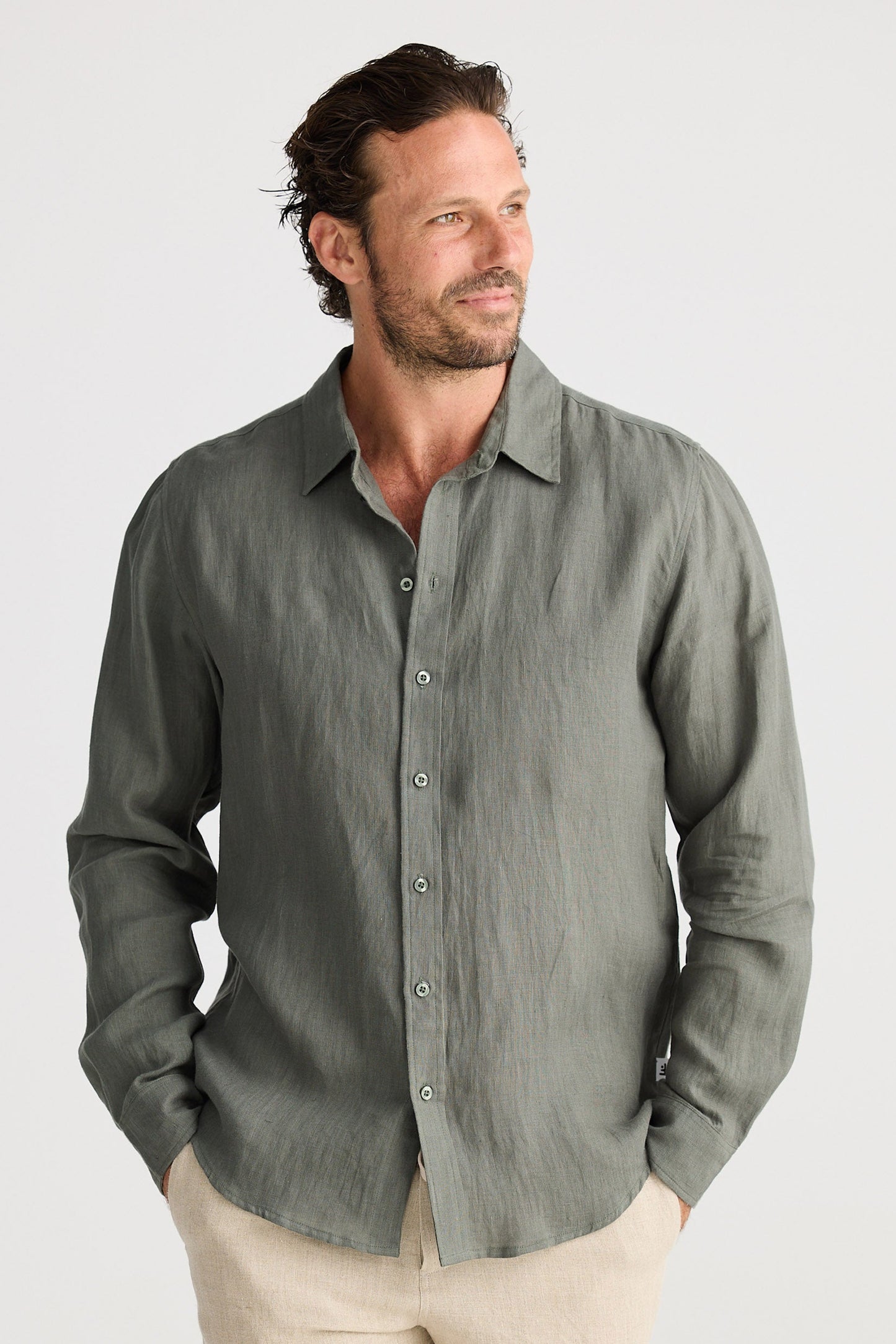Man wearing a green button-up shirt and beige shorts on a white background