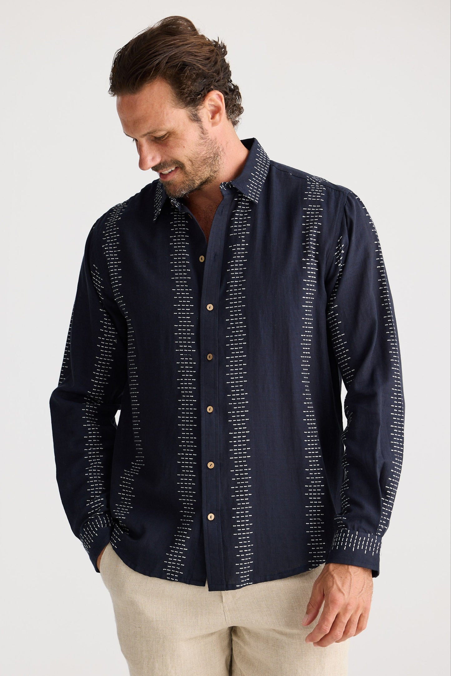 Man wearing a dark blue patterned shirt and beige shorts on a white background