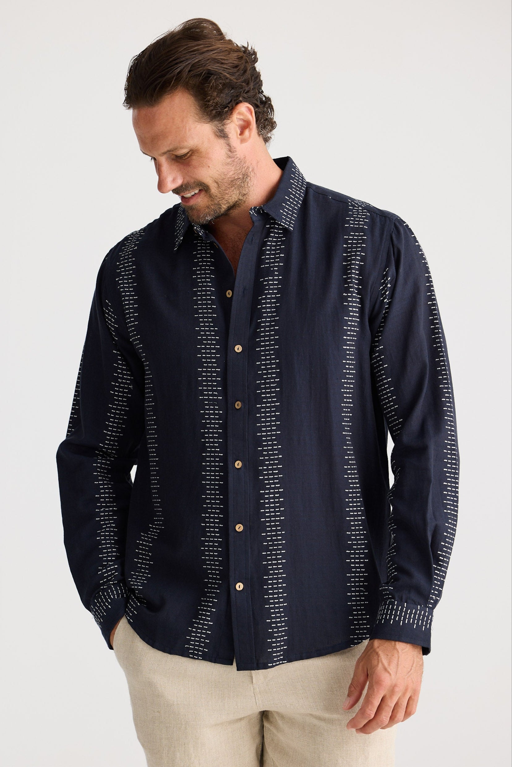 Man wearing a dark blue patterned shirt and beige shorts on a white background