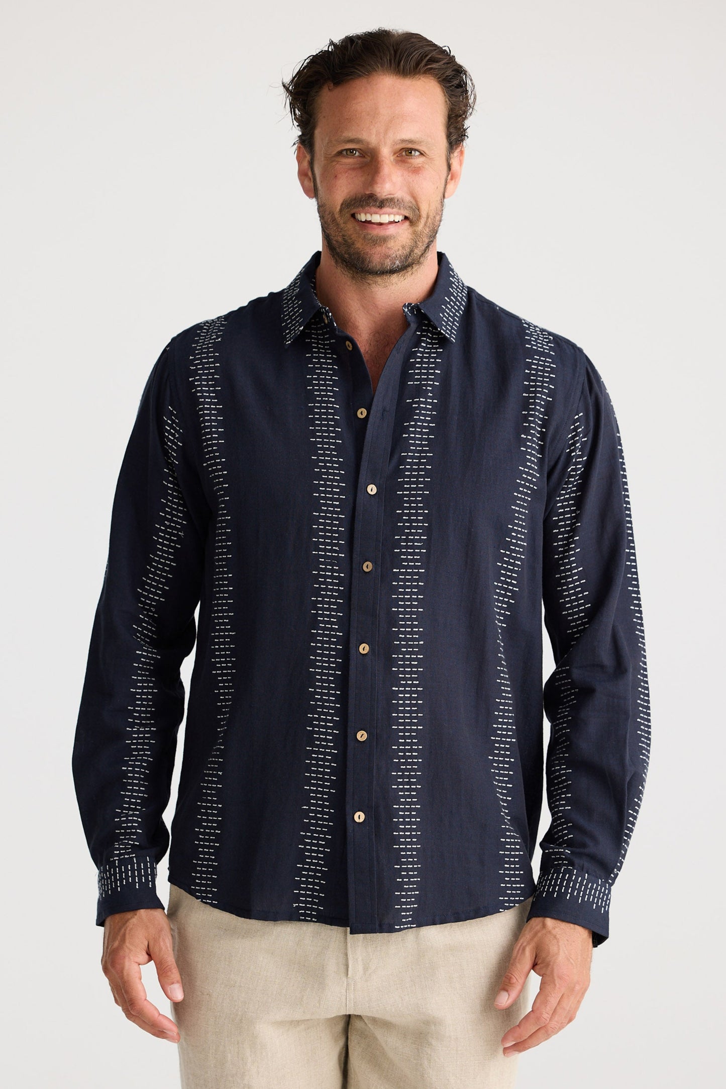 Man wearing a navy patterned shirt and beige shorts on a white background