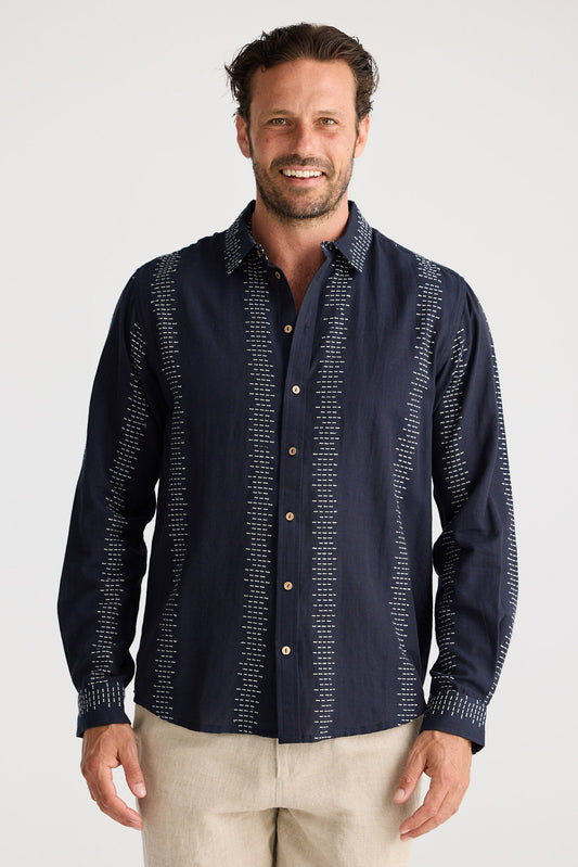 Man wearing a navy patterned shirt and beige shorts on a white background