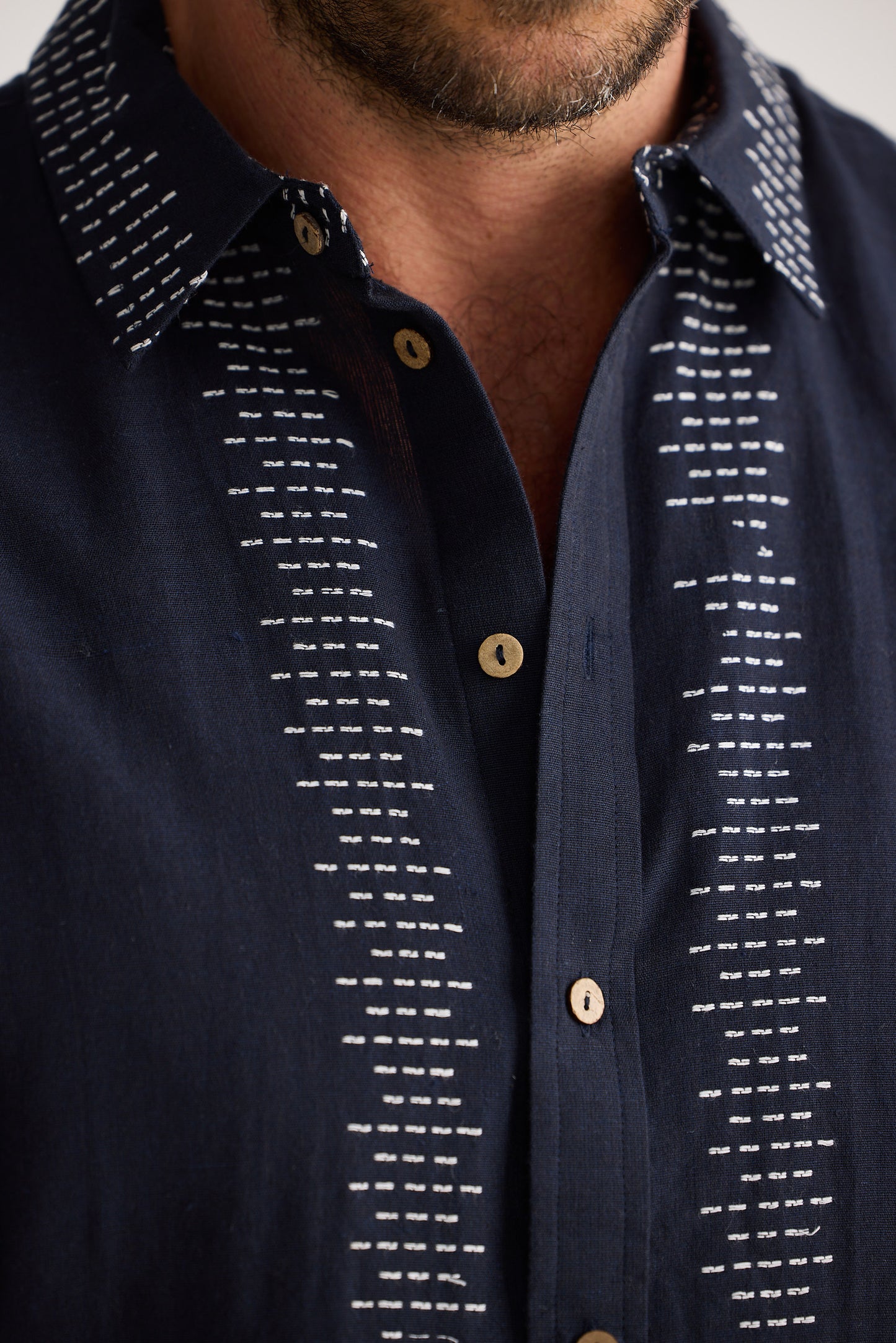 Navy blue shirt with white pattern and gold buttons on a neutral background