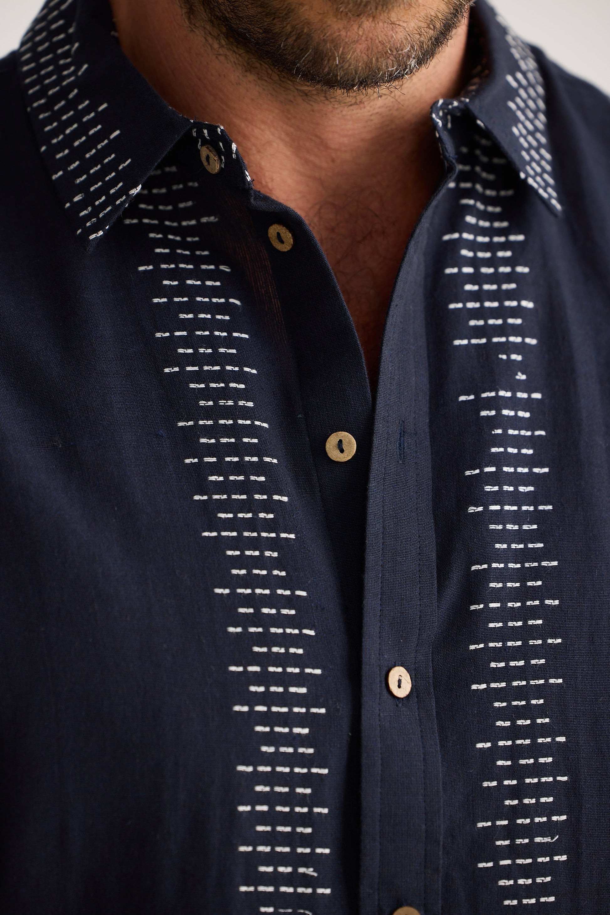 Navy blue shirt with white pattern and gold buttons on a neutral background