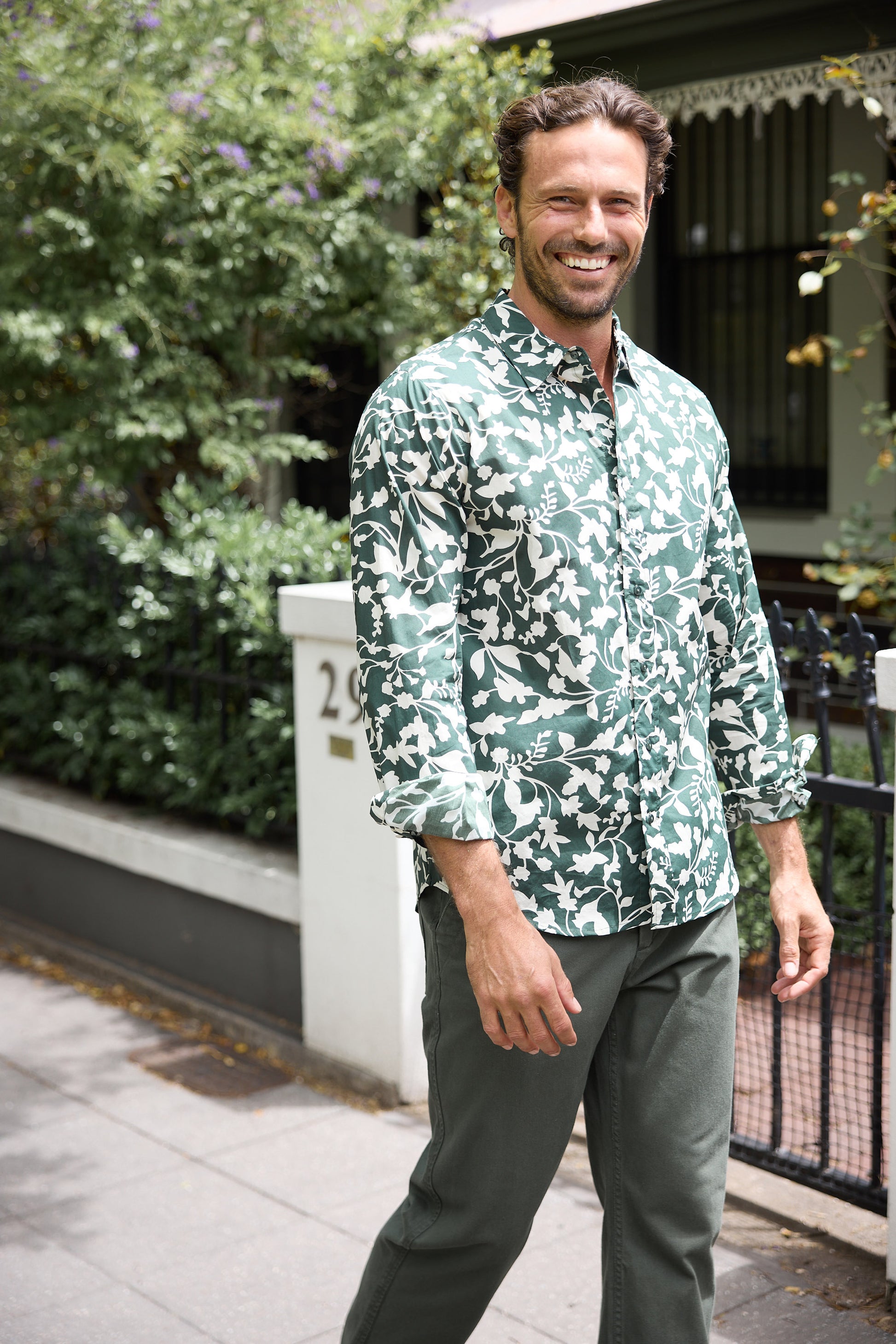 Man wearing a green patterned shirt standing outdoors with greenery in the background