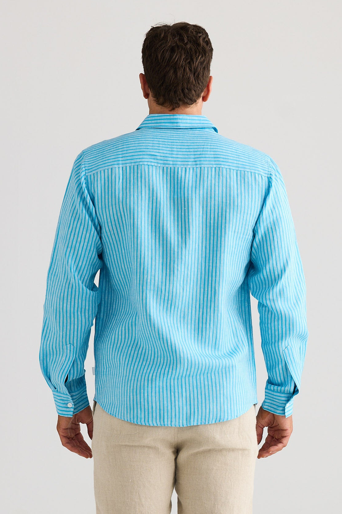 Man wearing a blue striped shirt and beige pants against a white background