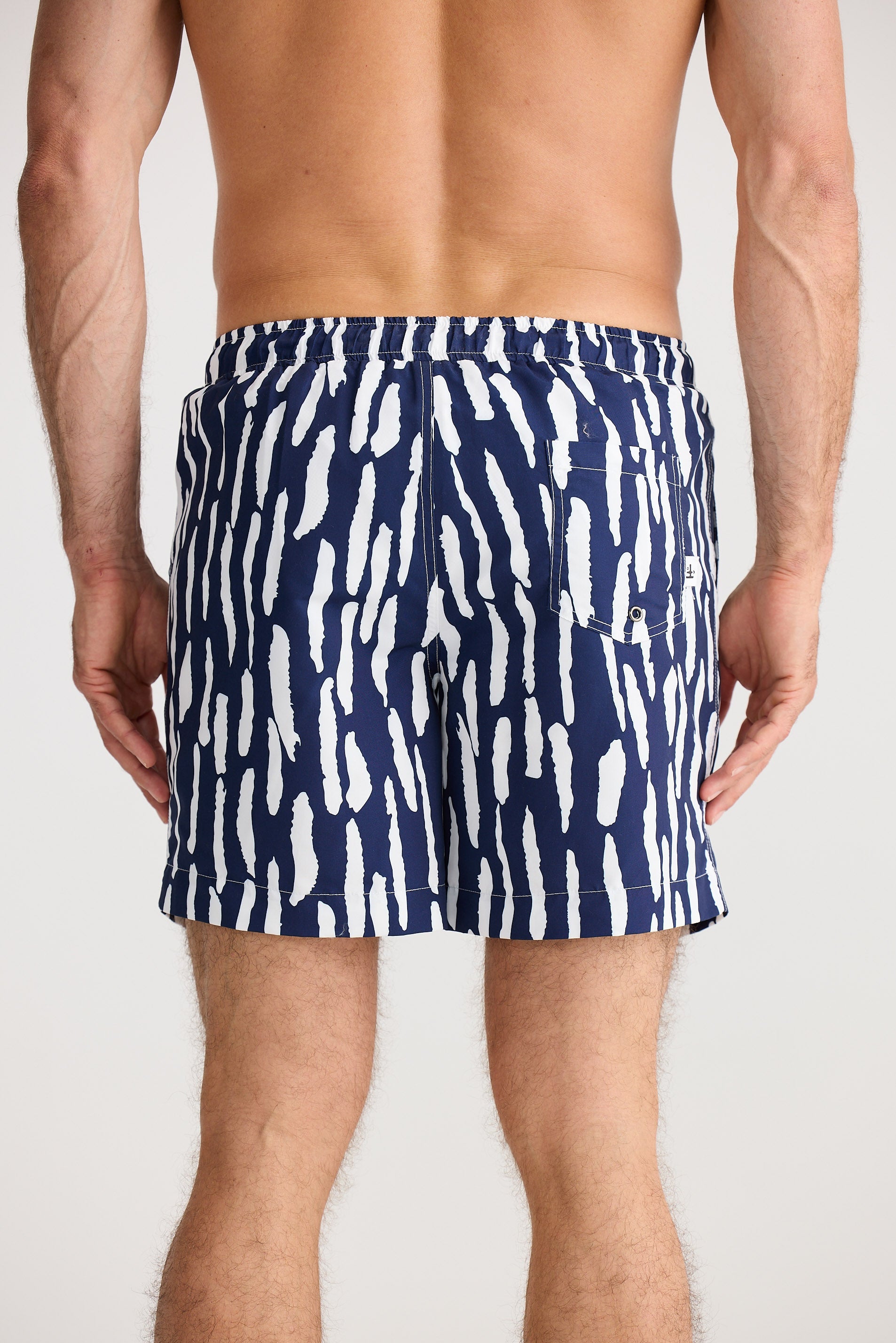 Person wearing navy swim shorts with white abstract pattern on a plain background