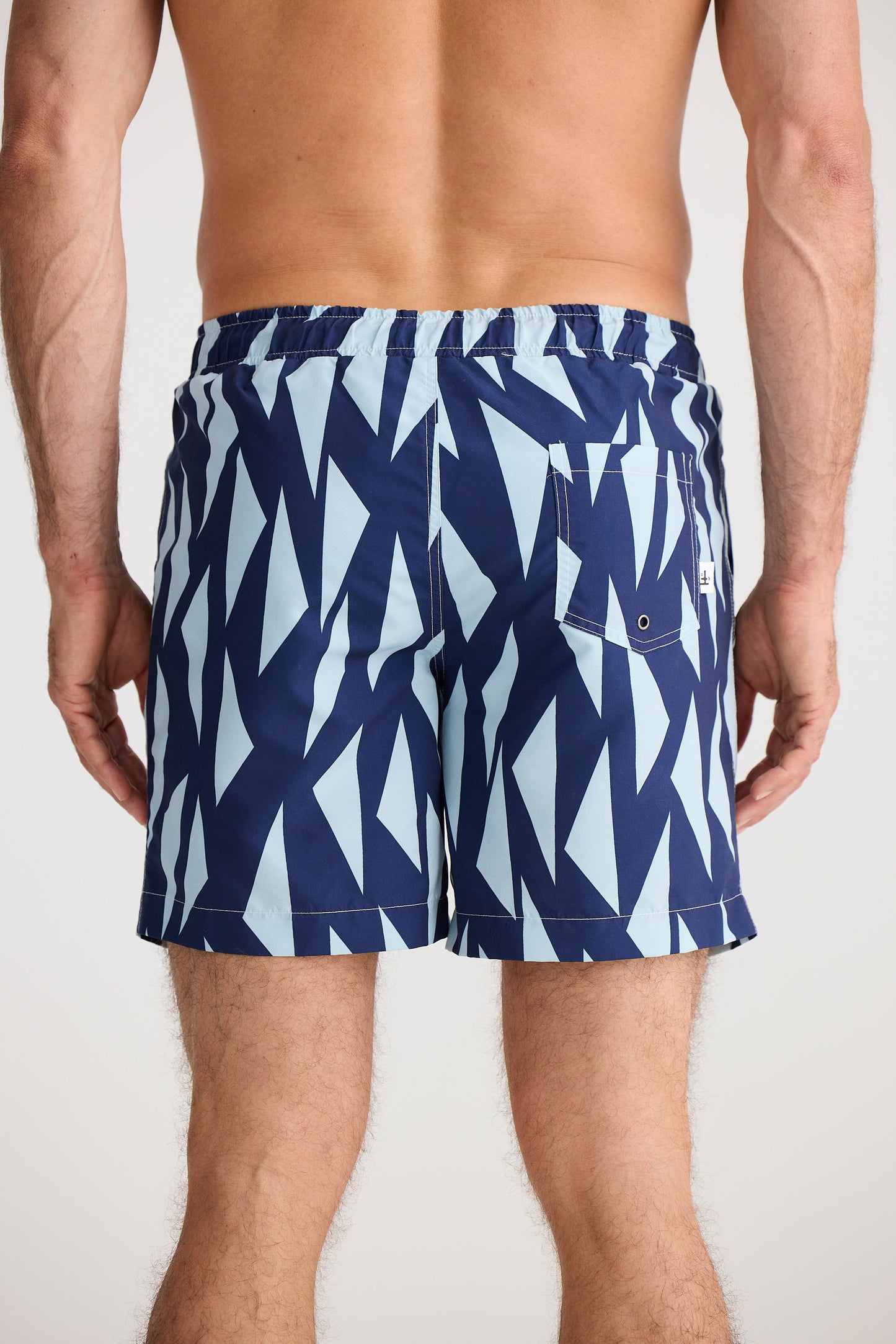 Person wearing blue and white patterned swim shorts on a plain background
