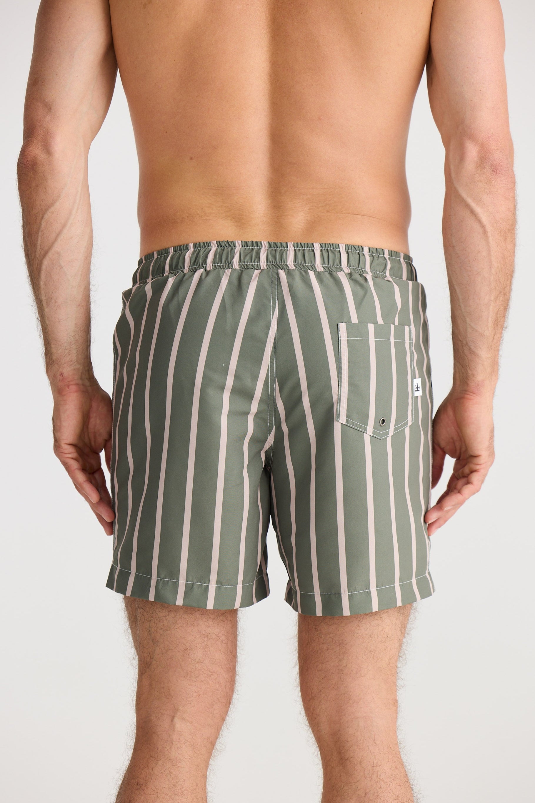 Person wearing green and white striped swim shorts on a plain background