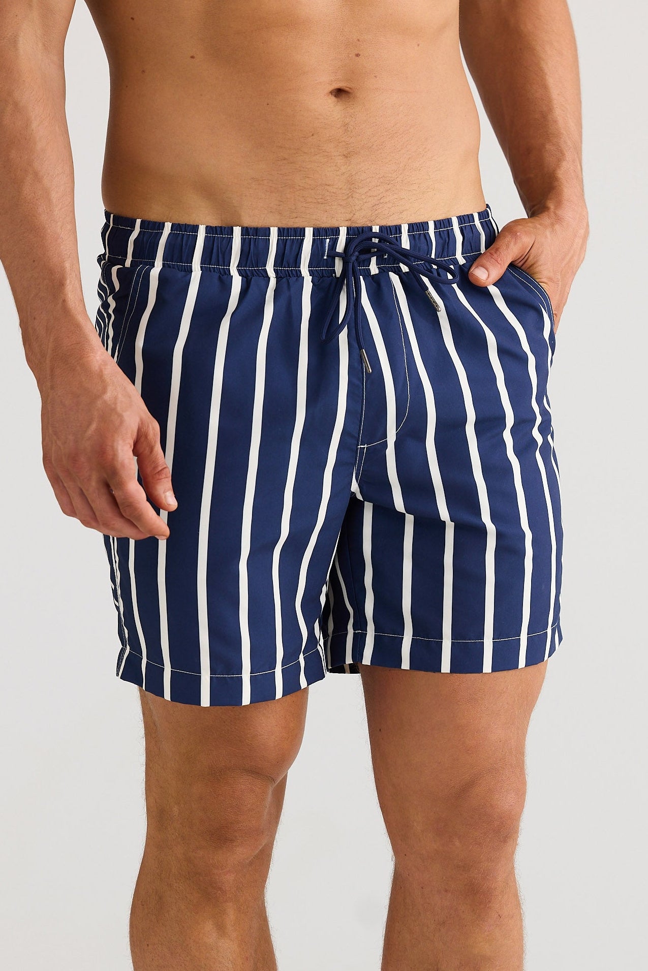 Man wearing navy and white striped swim shorts on a plain background
