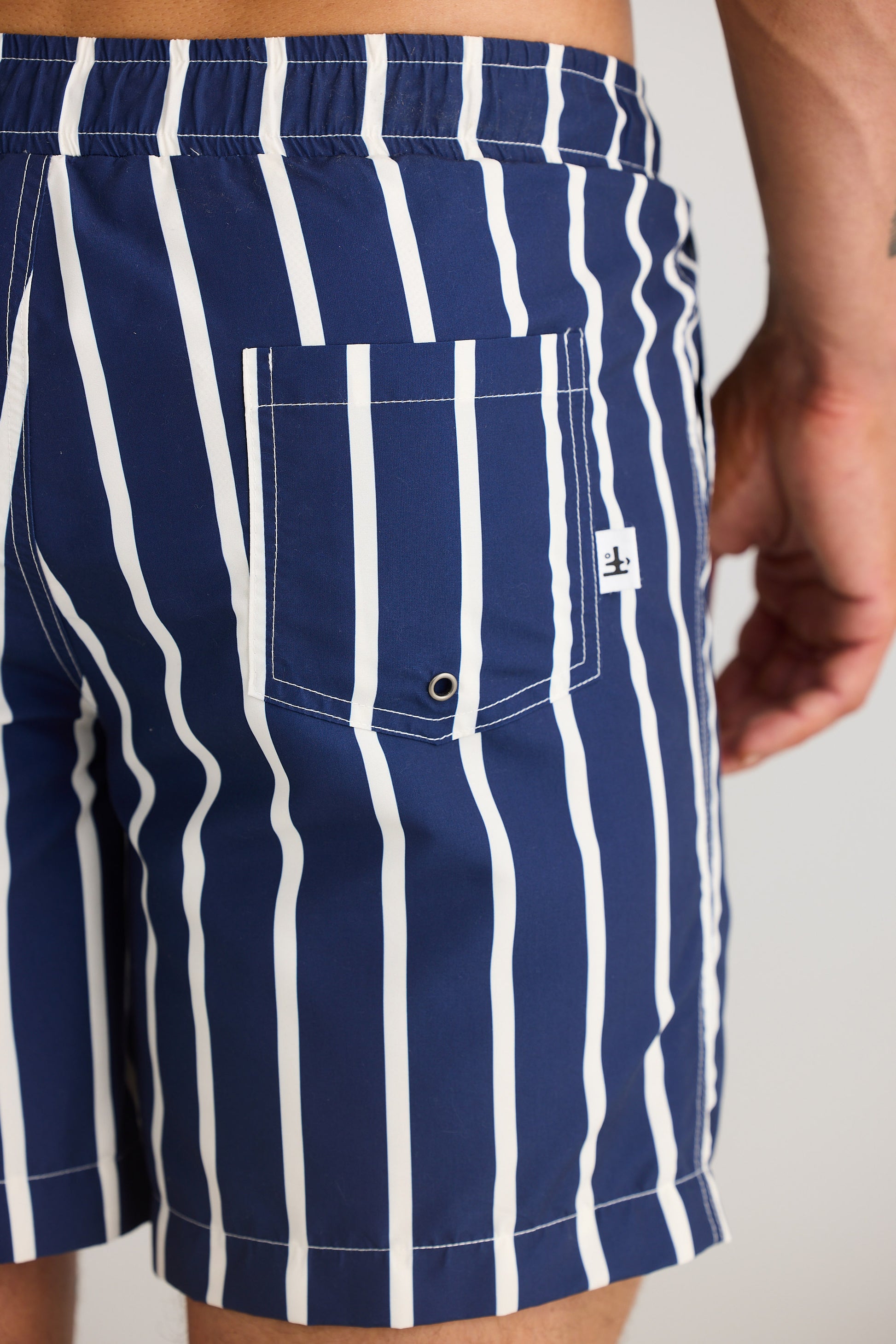 Navy and white striped swim shorts with a brand logo on a neutral background