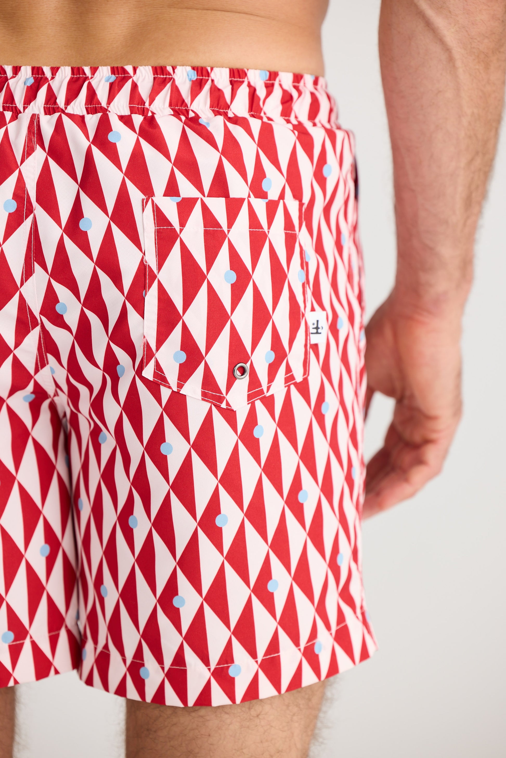 Red and white geometric patterned swim shorts on a plain background