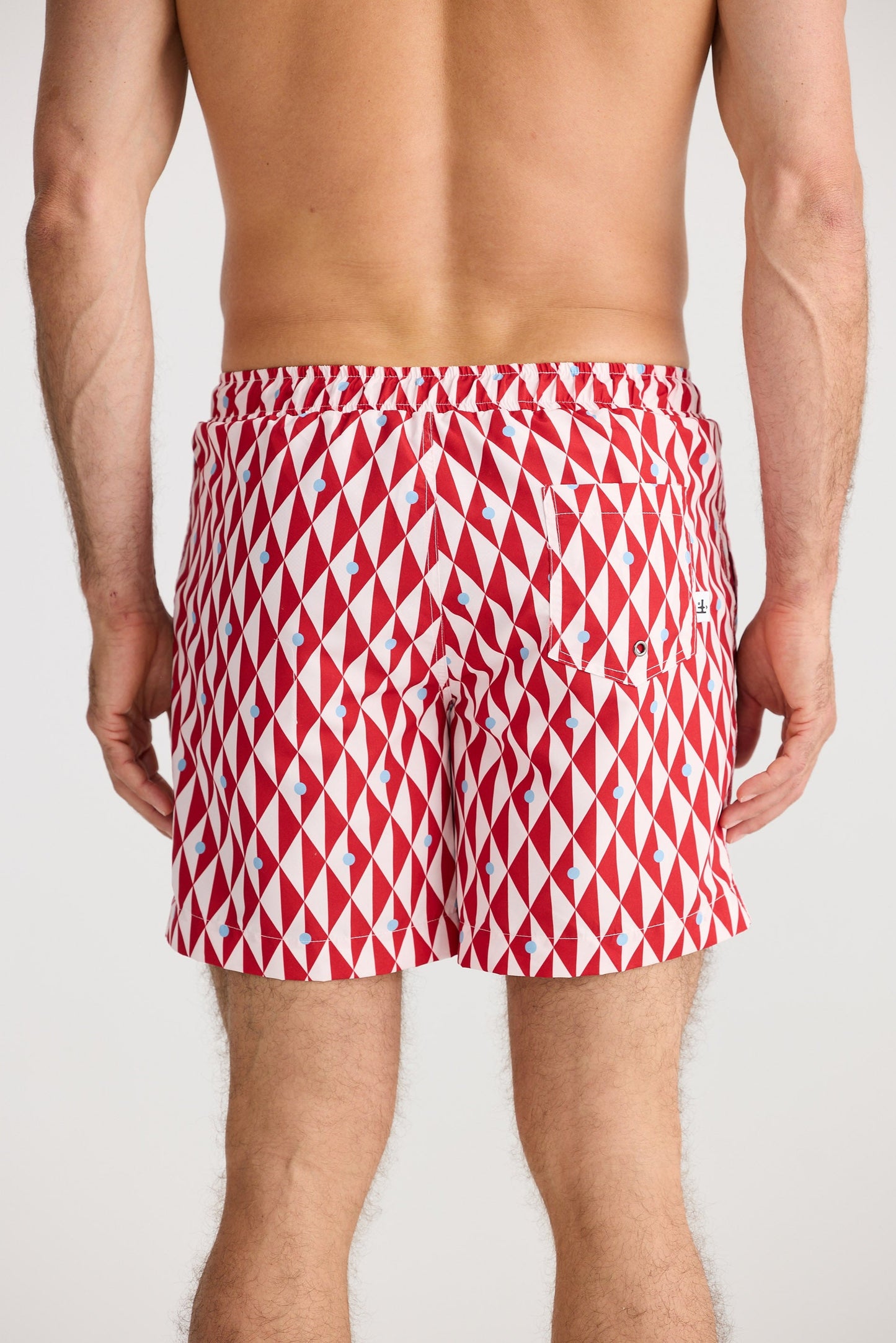 Red and white patterned swim shorts worn by a person on a plain background