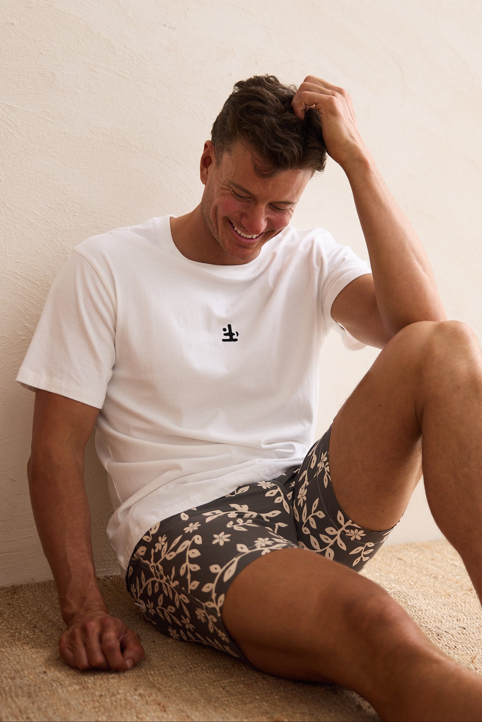 Man sitting on a beige couch wearing a white t-shirt and patterned shorts.