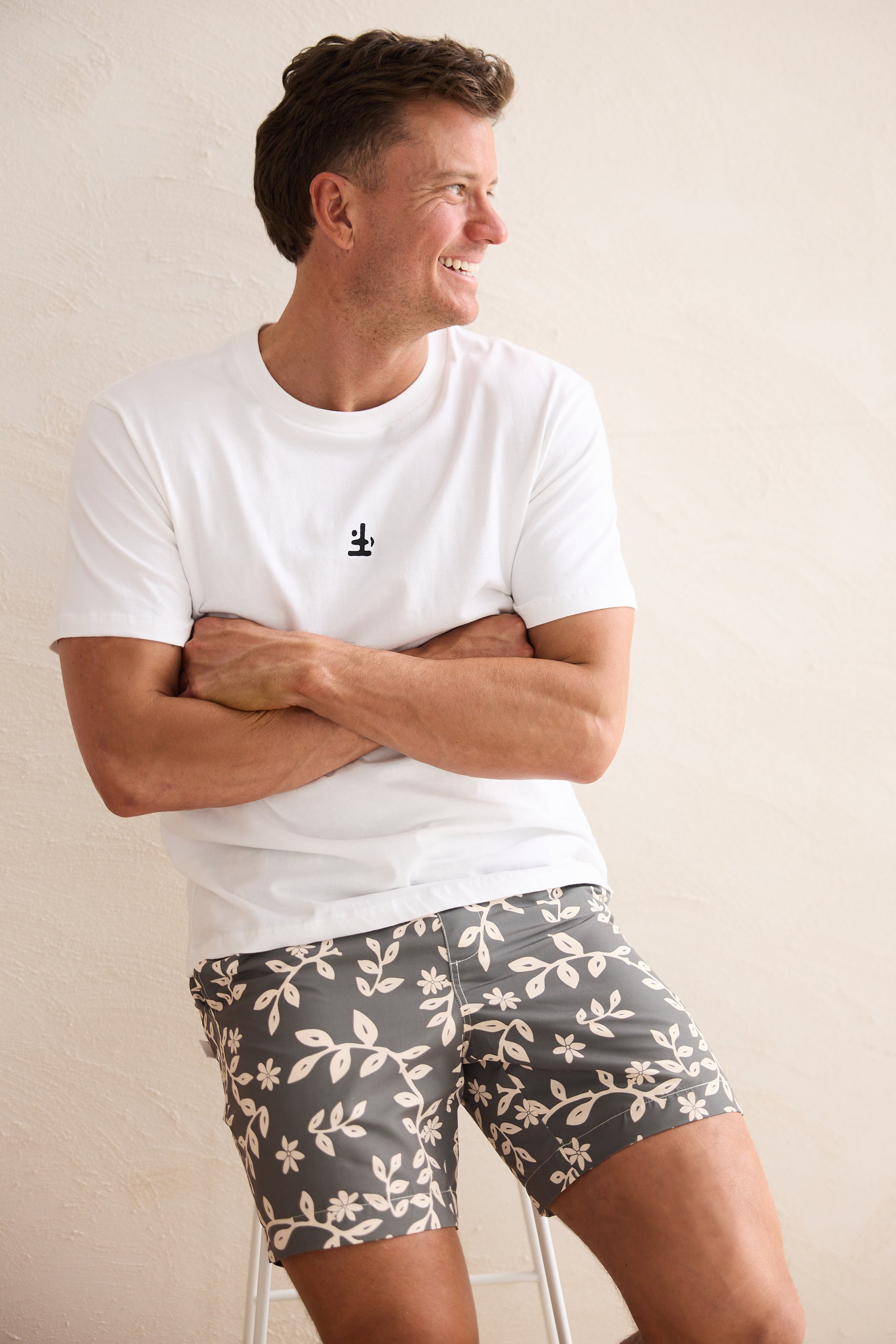 Man wearing a white t-shirt and patterned shorts against a plain background