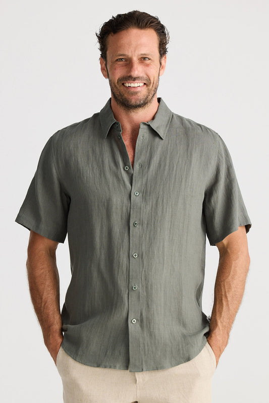 Man wearing a green short-sleeve shirt and beige shorts on a white background
