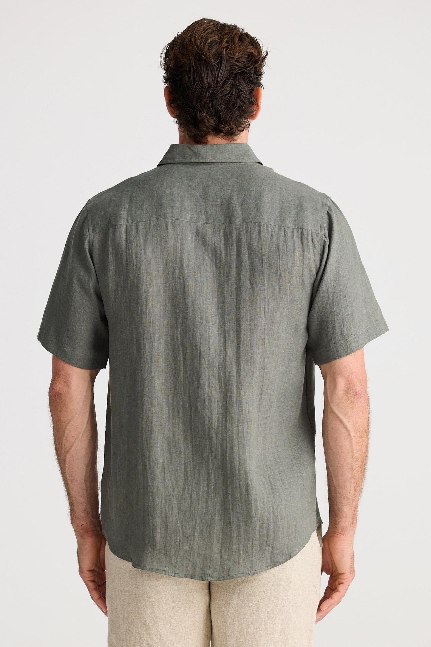 Man wearing a green short-sleeve shirt and beige shorts on a white background