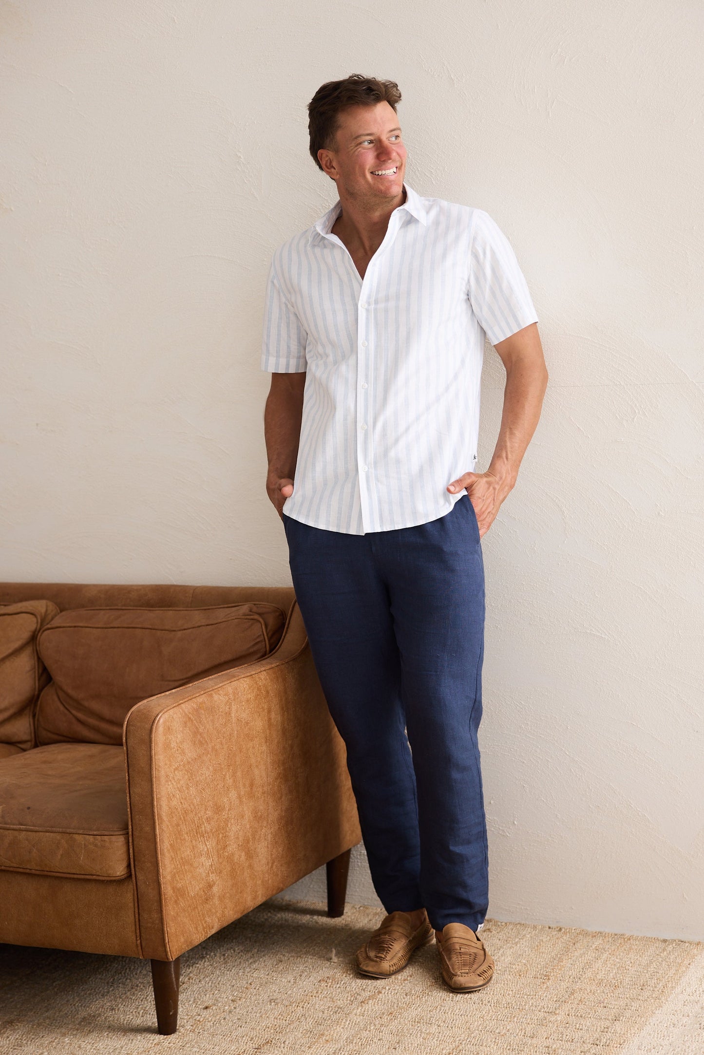Man wearing a white shirt and blue pants standing in a room with a brown couch.