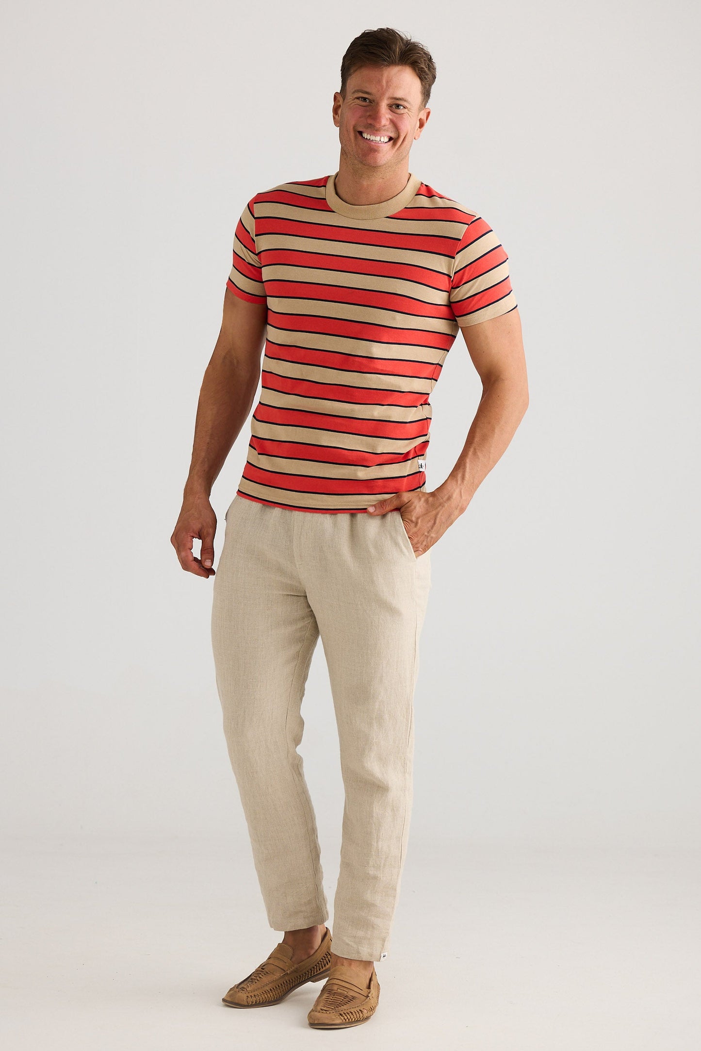 Man wearing a red and beige striped shirt with beige pants on a white background