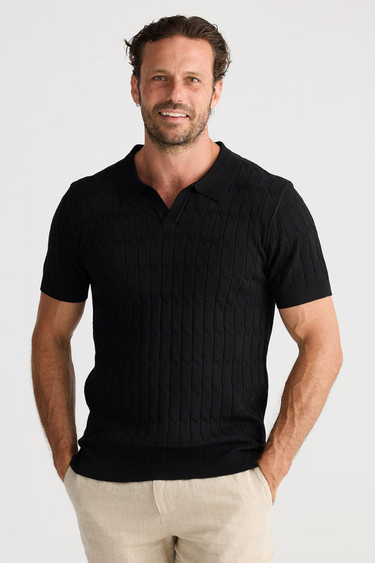 Man wearing a black polo shirt and beige shorts on a white background