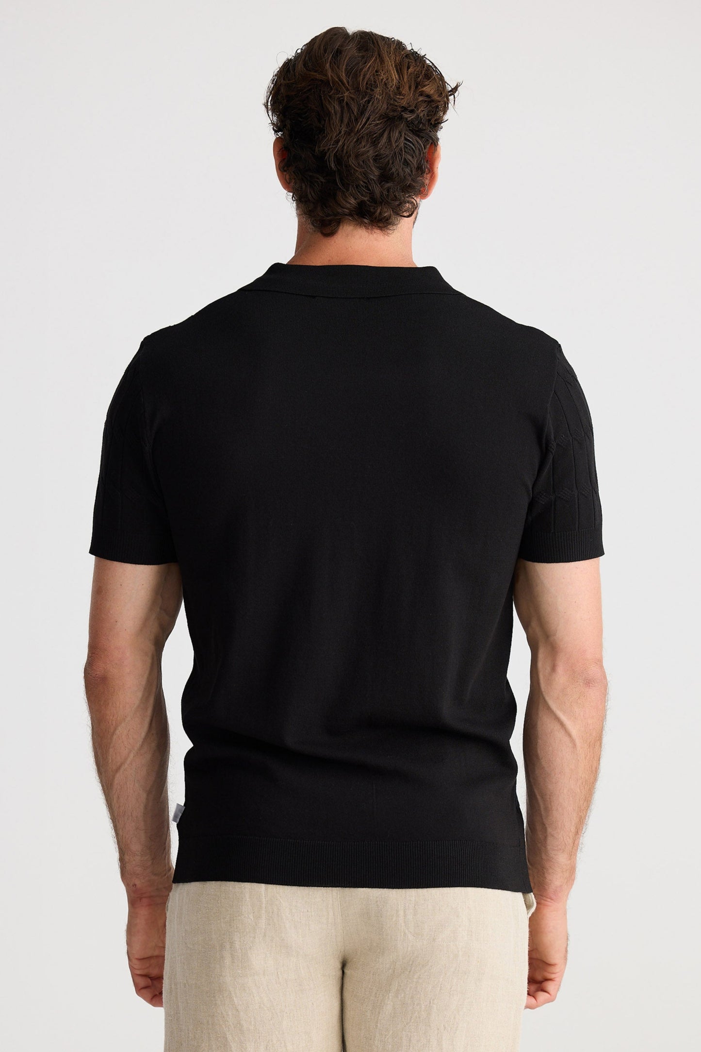 Man wearing a black t-shirt and beige shorts on a white background