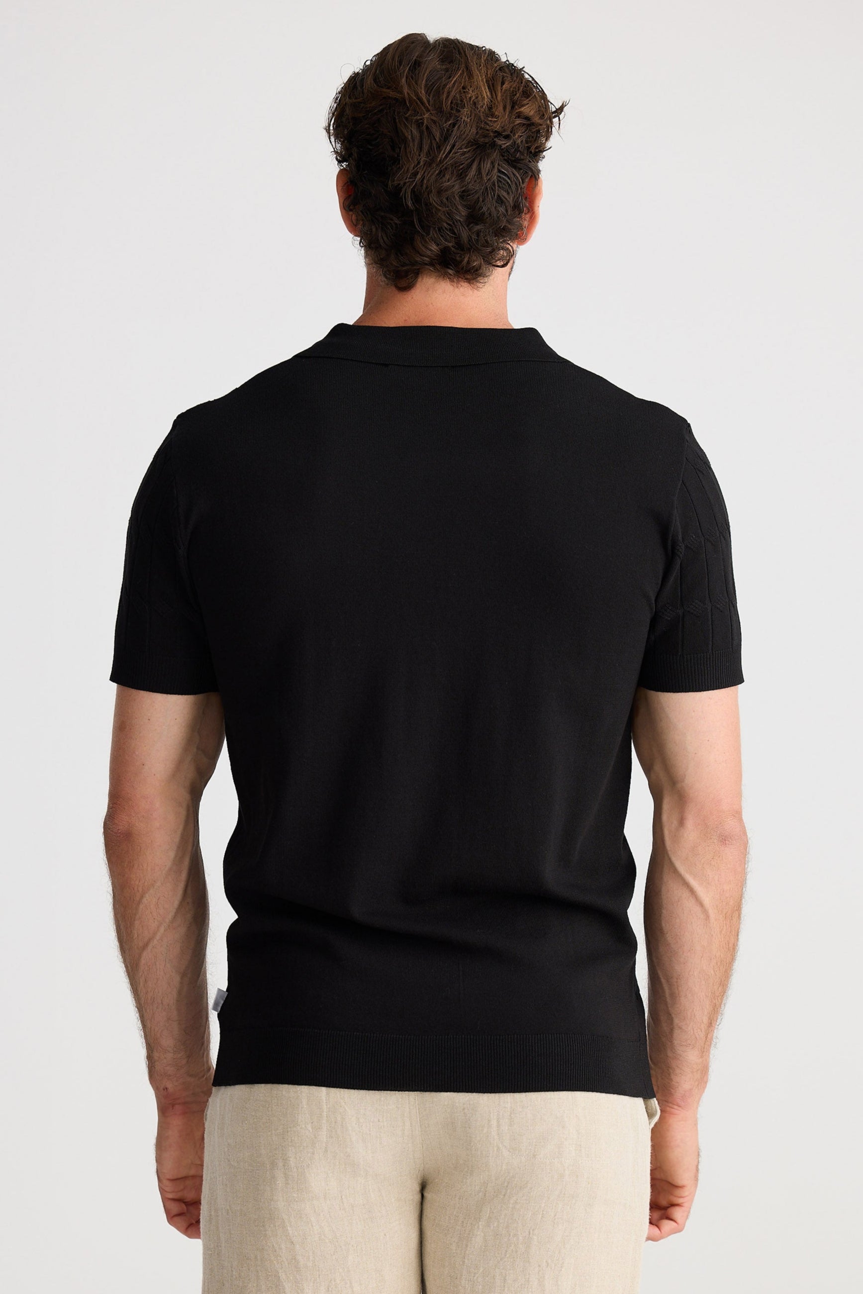 Man wearing a black t-shirt and beige shorts on a white background
