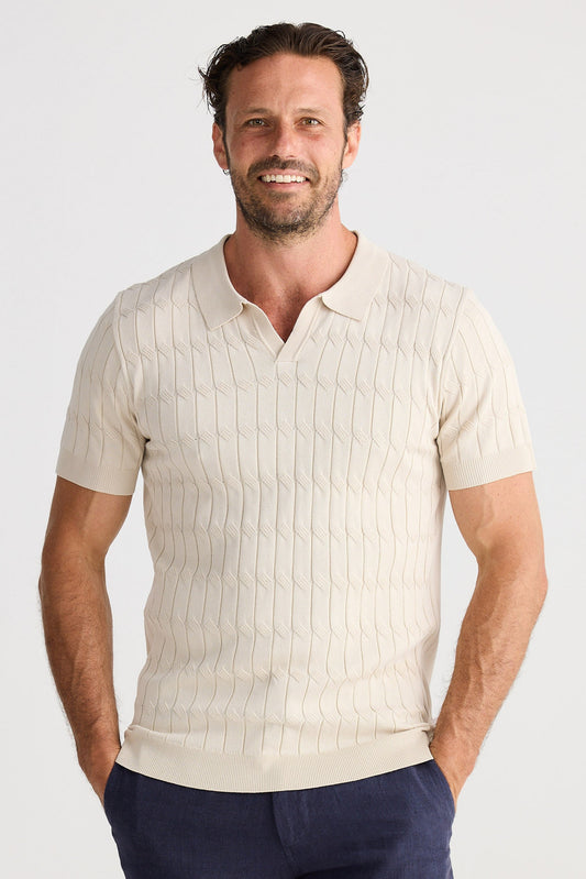 Man wearing a cream knit shirt and navy shorts on a white background