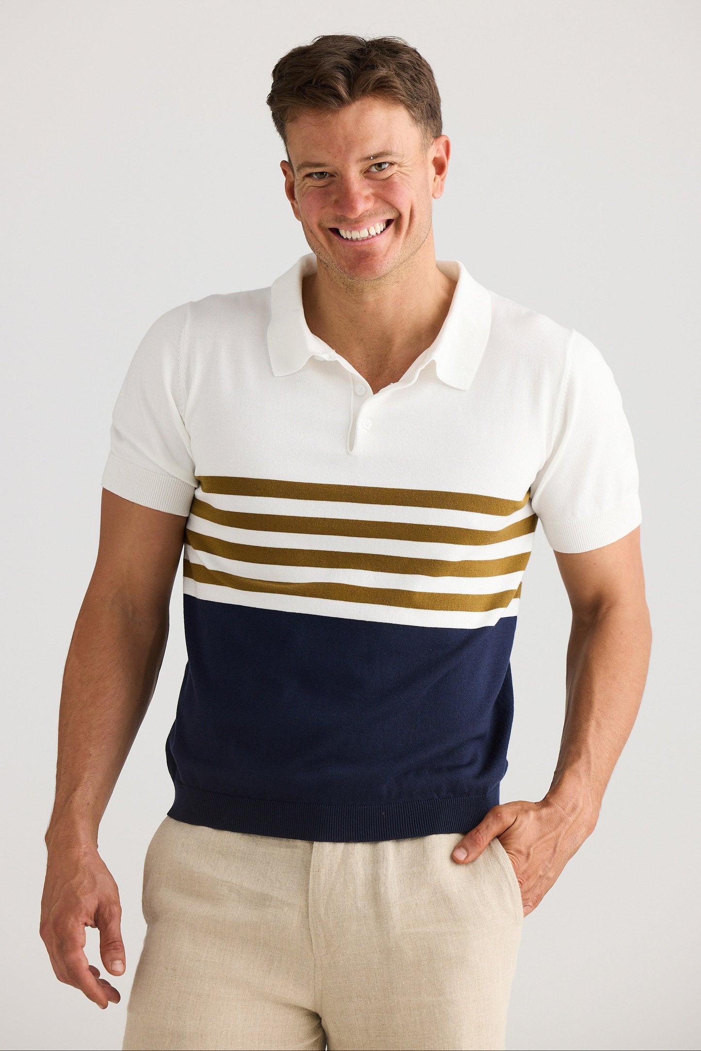 Man wearing a white polo shirt with gold and navy stripes on a plain background