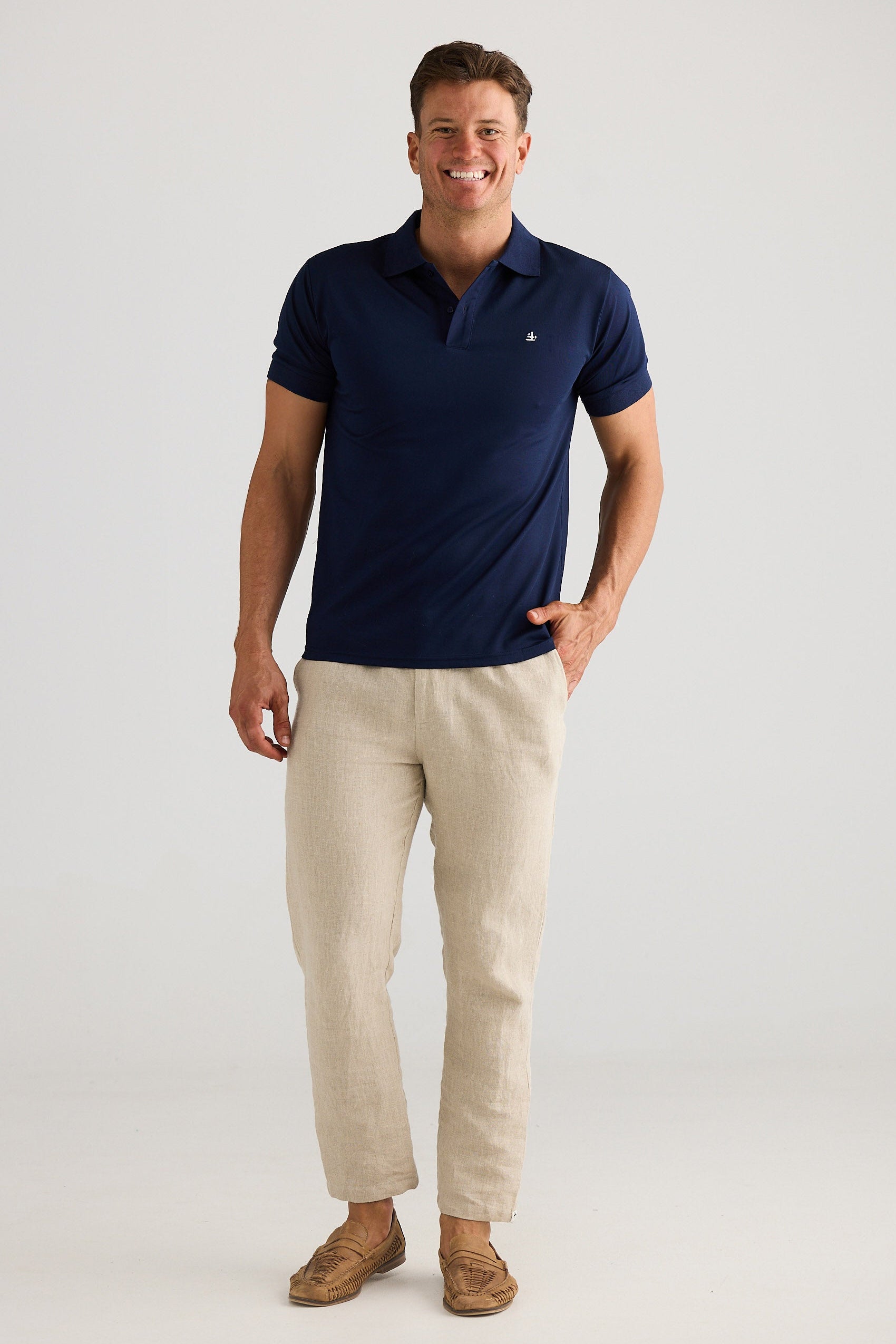 Man wearing a navy polo shirt and beige pants on a white background